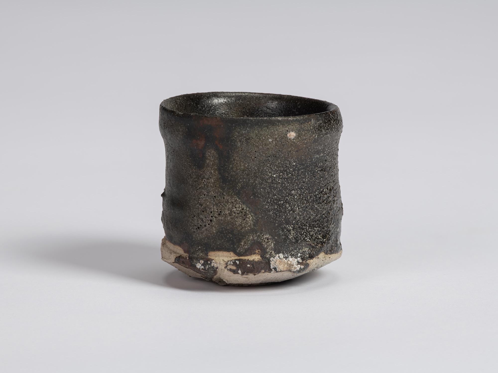 Kuro Guinomi by Shiro Tsujimura, with a tall cylindrical form, irregular rim, and textured black...