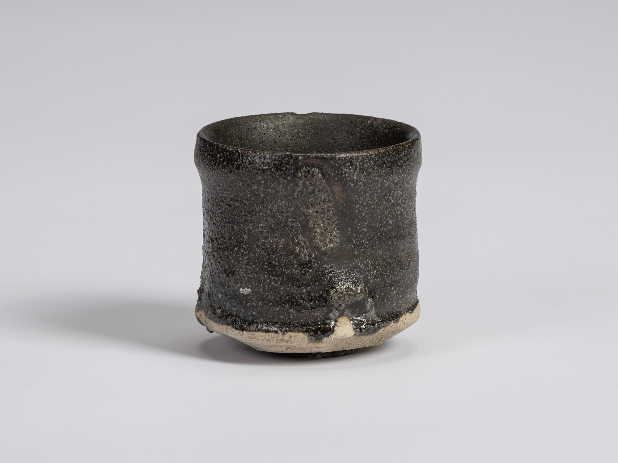 Kuro Guinomi by Shiro Tsujimura, with a tall cylindrical form, irregular rim, and textured black...