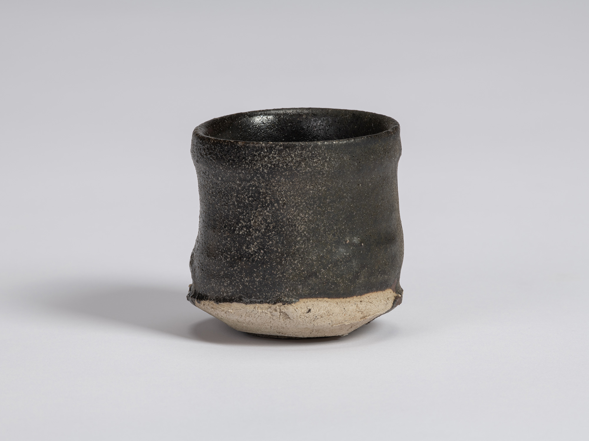 Kuro Guinomi by Shiro Tsujimura, with a tall cylindrical form, irregular rim, and textured black...