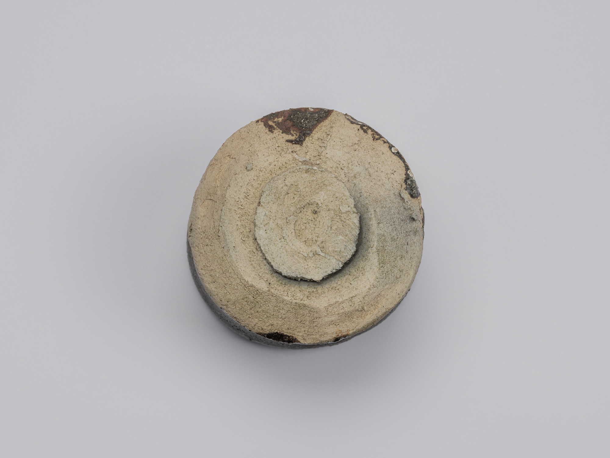 Underside view of Kuro Guinomi by Shiro Tsujimura, showing a roughly finished circular foot surrounded...