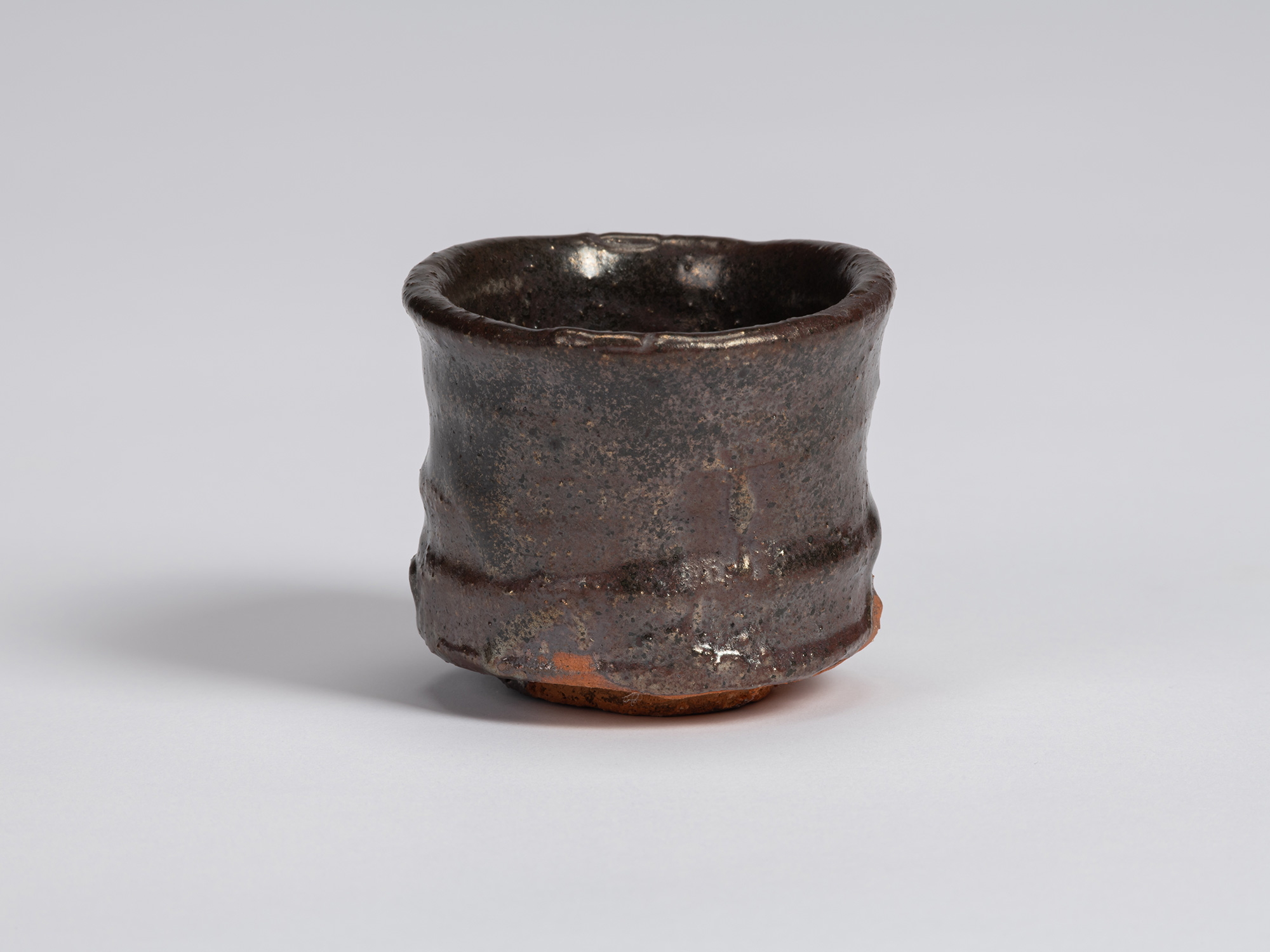 Kuro Guinomi by Shiro Tsujimura, with a cylindrical form, irregular rounded rim, and dark brown-black...