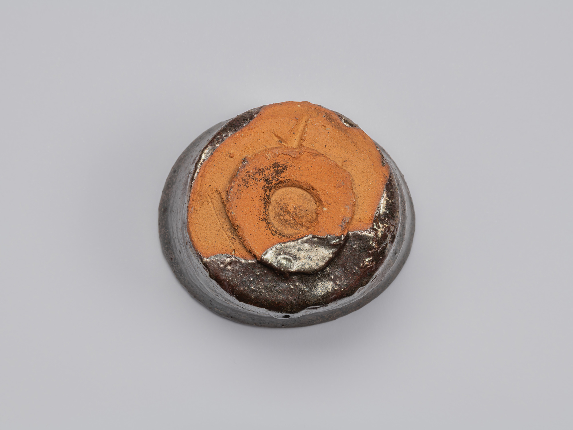 Underside view of Kuro Guinomi by Shiro Tsujimura, showing an exposed orange clay base and circular...