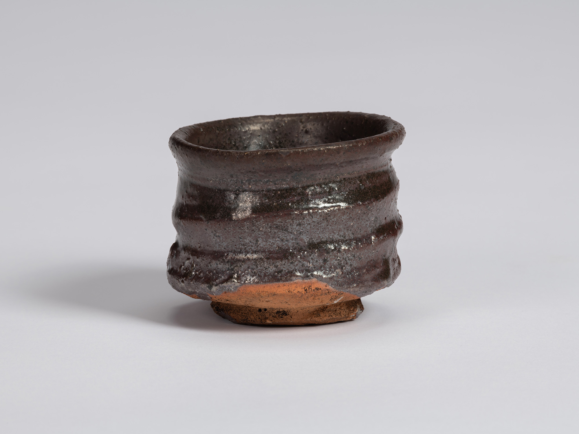 Kuro Guinomi by Shiro Tsujimura, with a slightly flared irregular rim, dark brown-black glaze,...