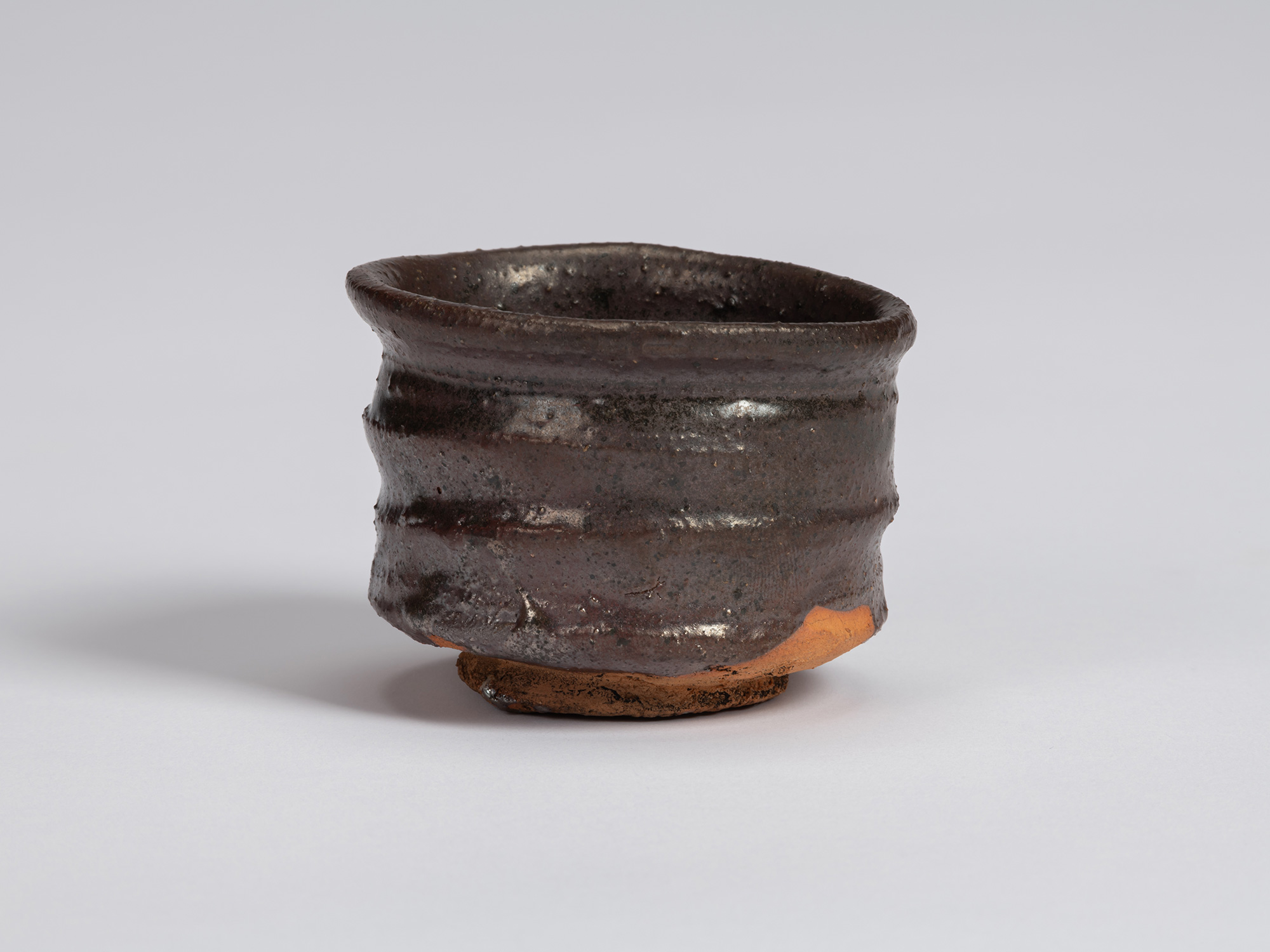 Kuro Guinomi by Shiro Tsujimura, with a slightly flared irregular rim, dark brown-black glaze,...