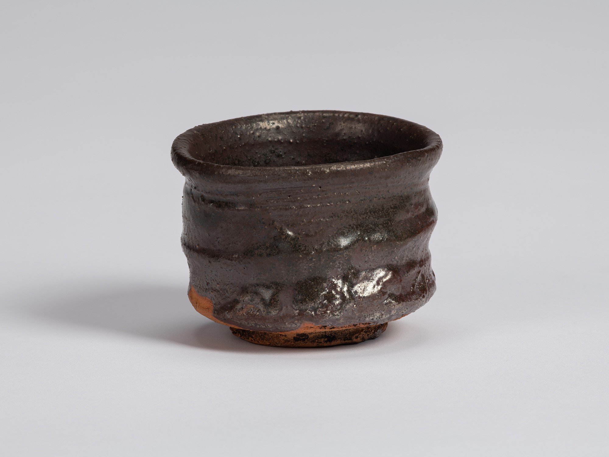 Kuro Guinomi by Shiro Tsujimura, with a slightly flared irregular rim, dark brown-black glaze,...