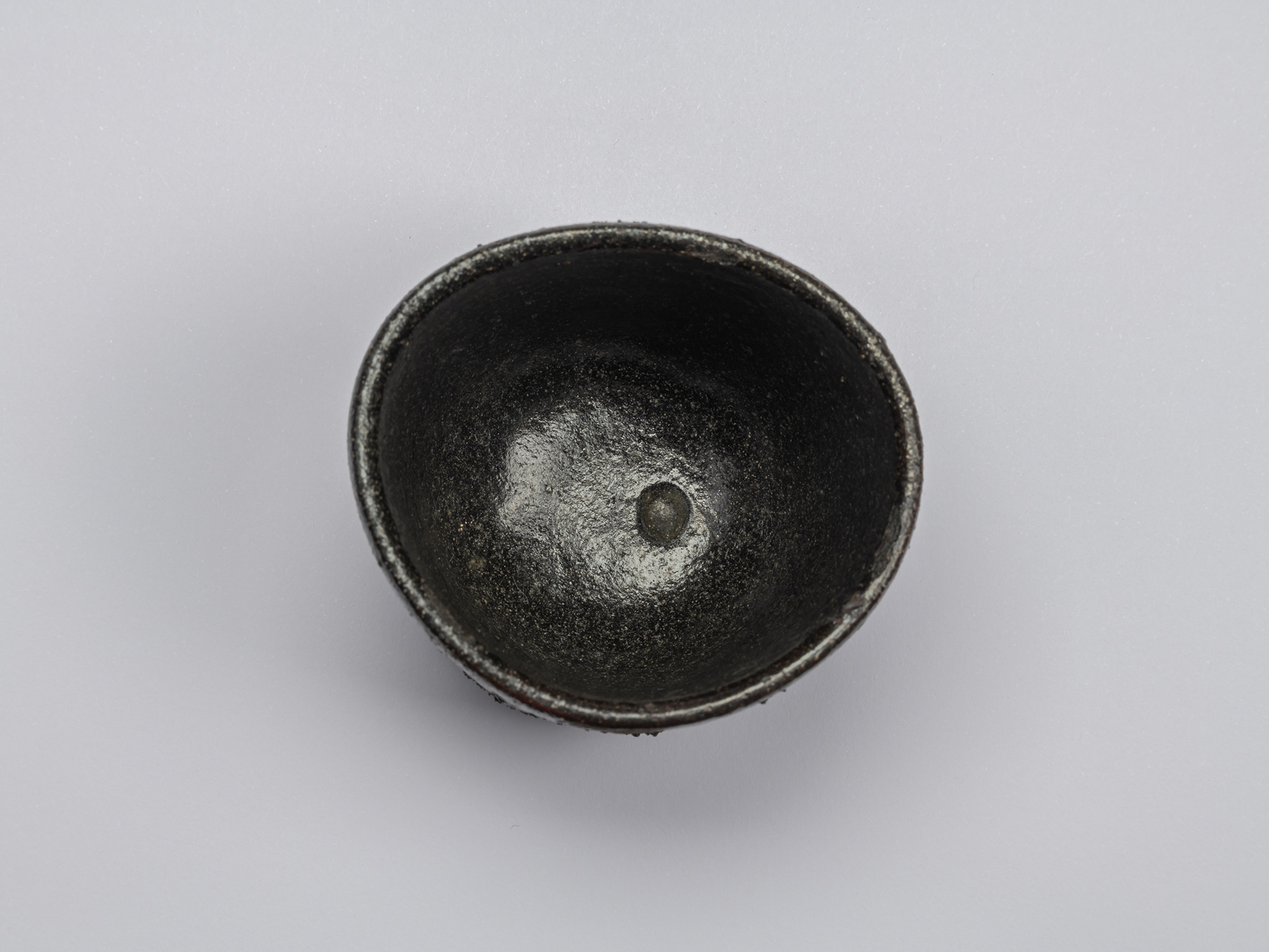 Kuro Guinomi by Shiro Tsujimura, overhead interior view, showing a dark black glazed surface with...