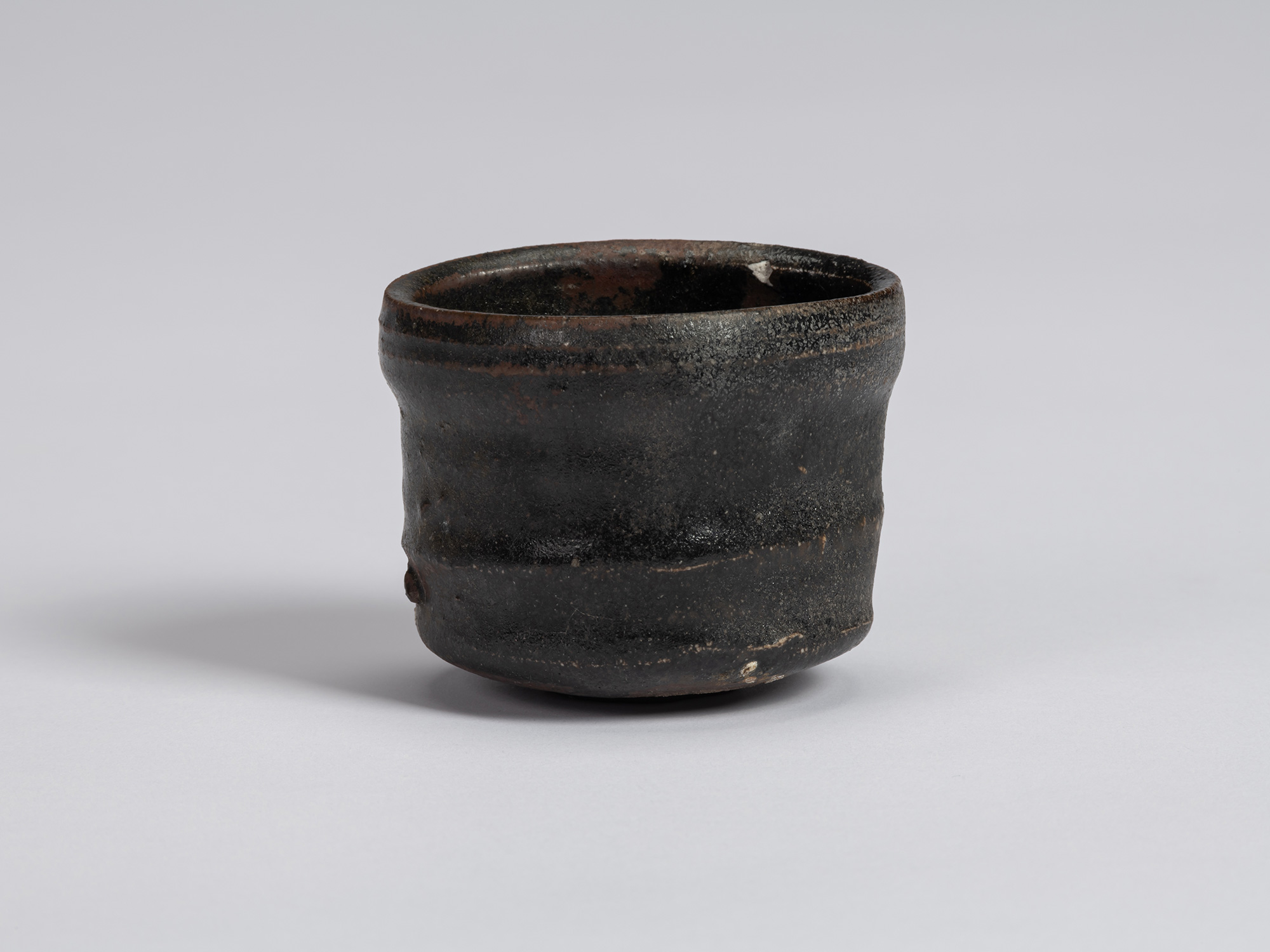 Kuro Guinomi by Shiro Tsujimura, front view, with a cylindrical form, irregular rim, horizontal...