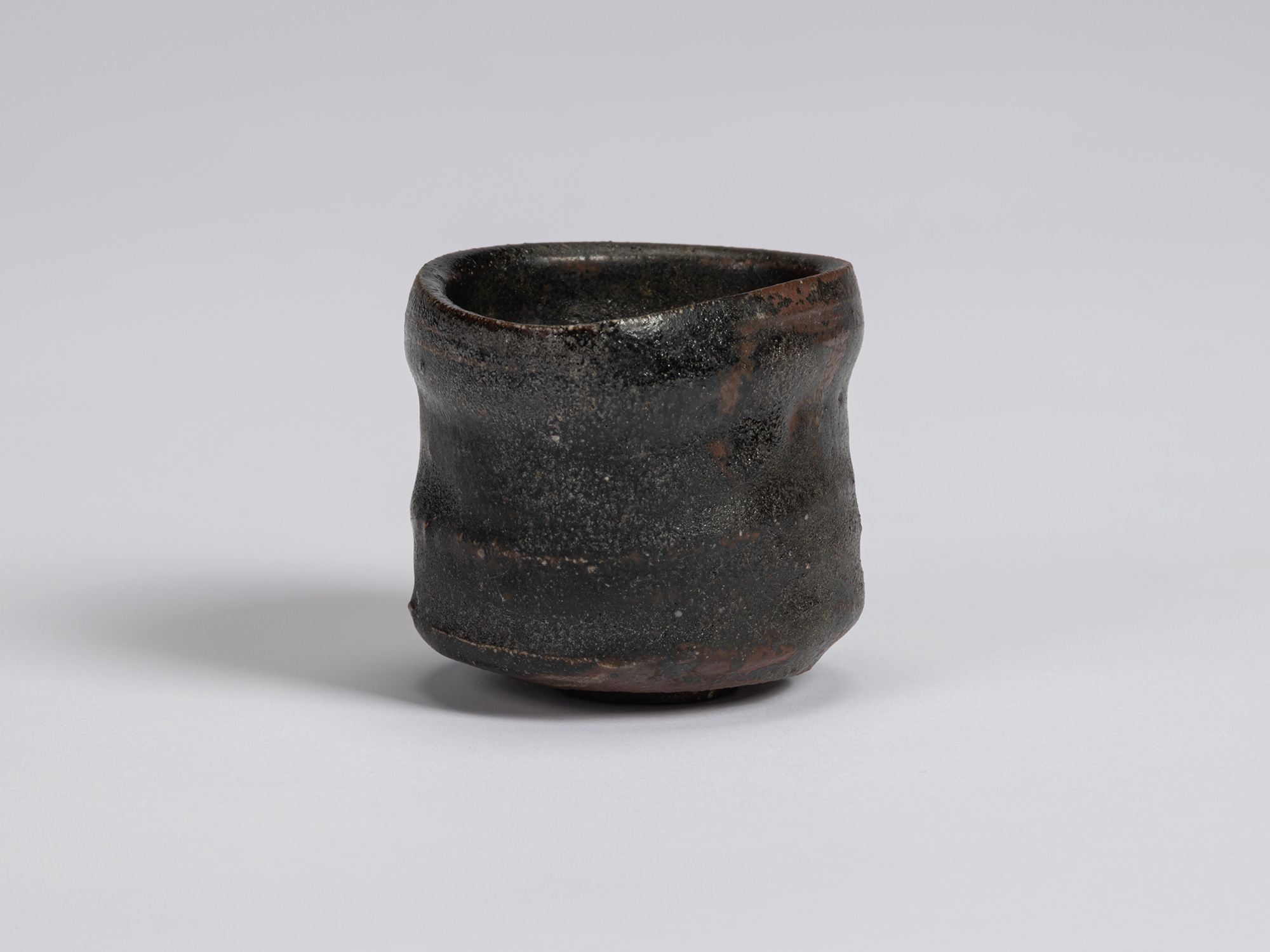 Kuro Guinomi by Shiro Tsujimura, front view, with a cylindrical form, irregular rim, horizontal...