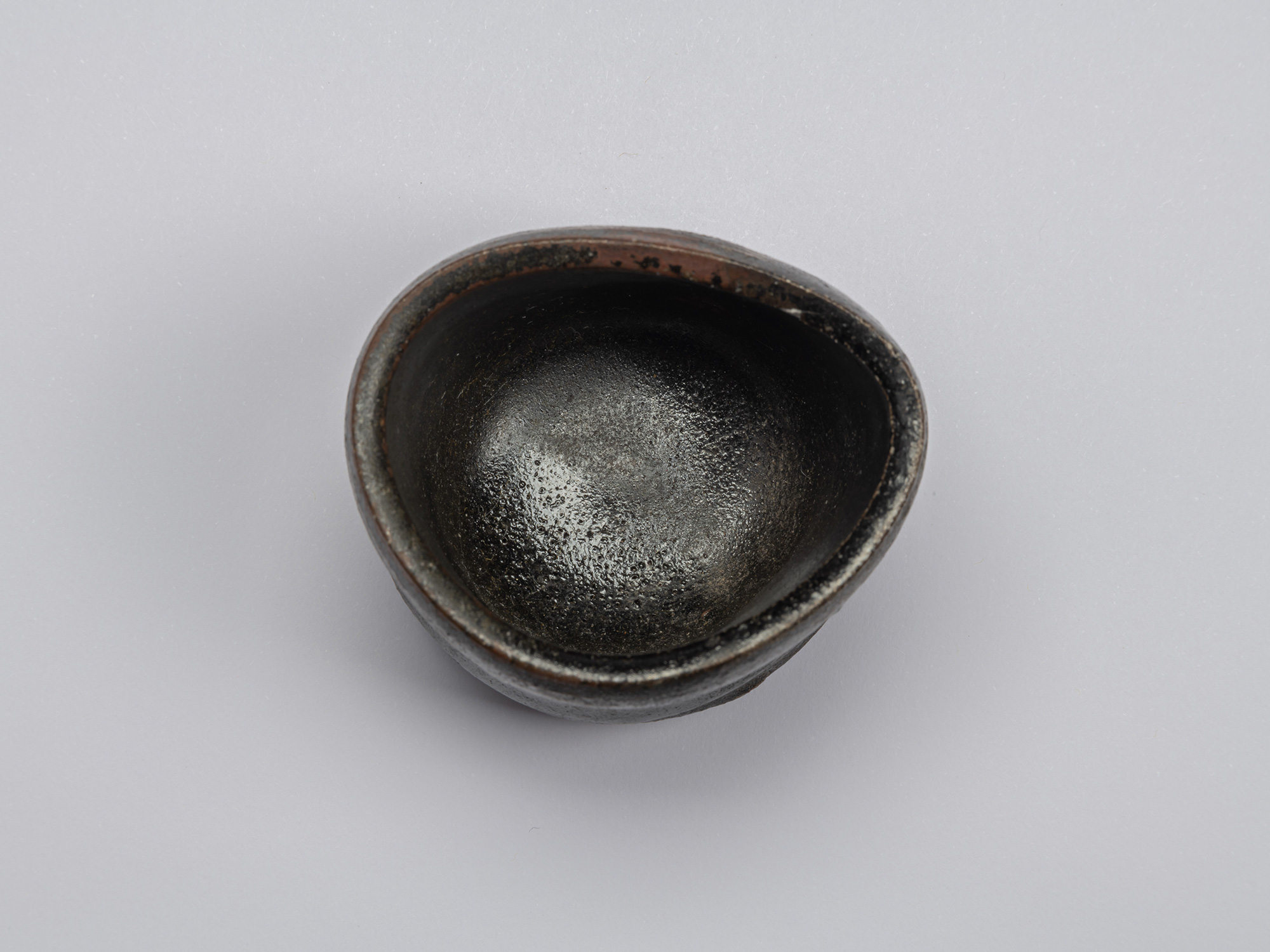 Kuro Guinomi by Shiro Tsujimura, overhead interior view, showing a dark glossy glaze with fine...