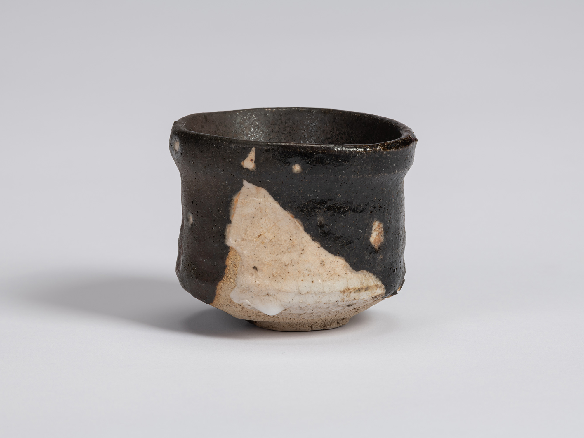 Kuro Guinomi by Shiro Tsujimura, front view, with an irregular cylindrical form, black glaze, and...