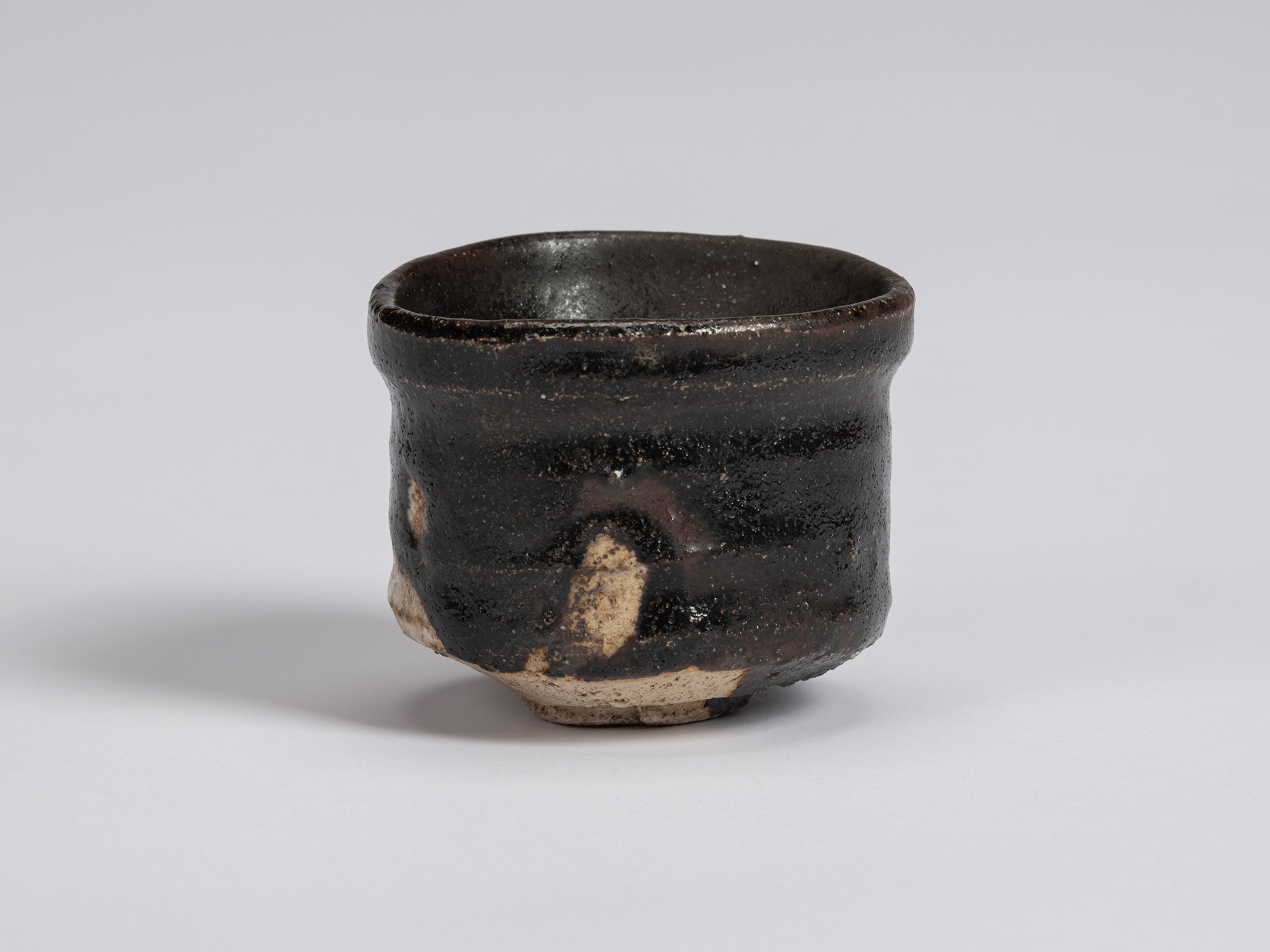 Kuro Guinomi by Shiro Tsujimura, alternate view, with glossy black glaze, horizontal ridges, reddish-brown...