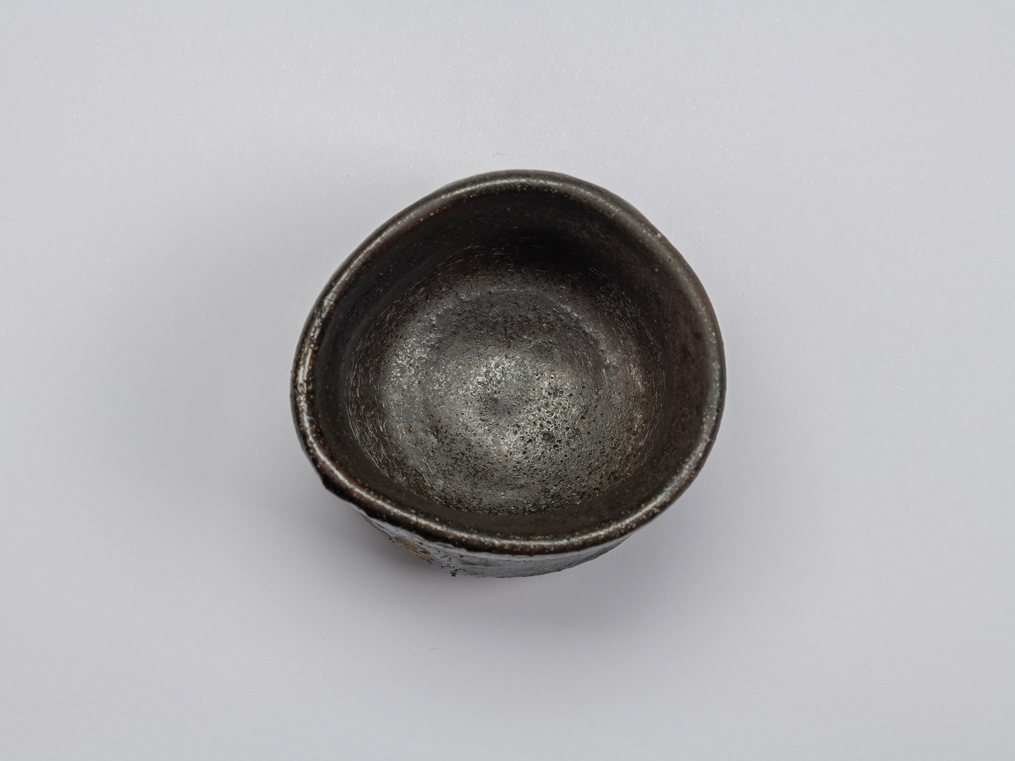 Kuro Guinomi by Shiro Tsujimura, overhead interior view, showing a dark black-brown glazed surface...