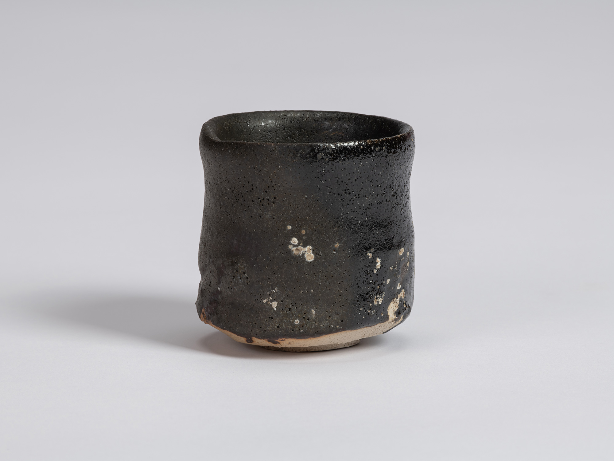 Kuro Guinomi by Shiro Tsujimura, front view, with a tall cylindrical form, subtly irregular rim,...