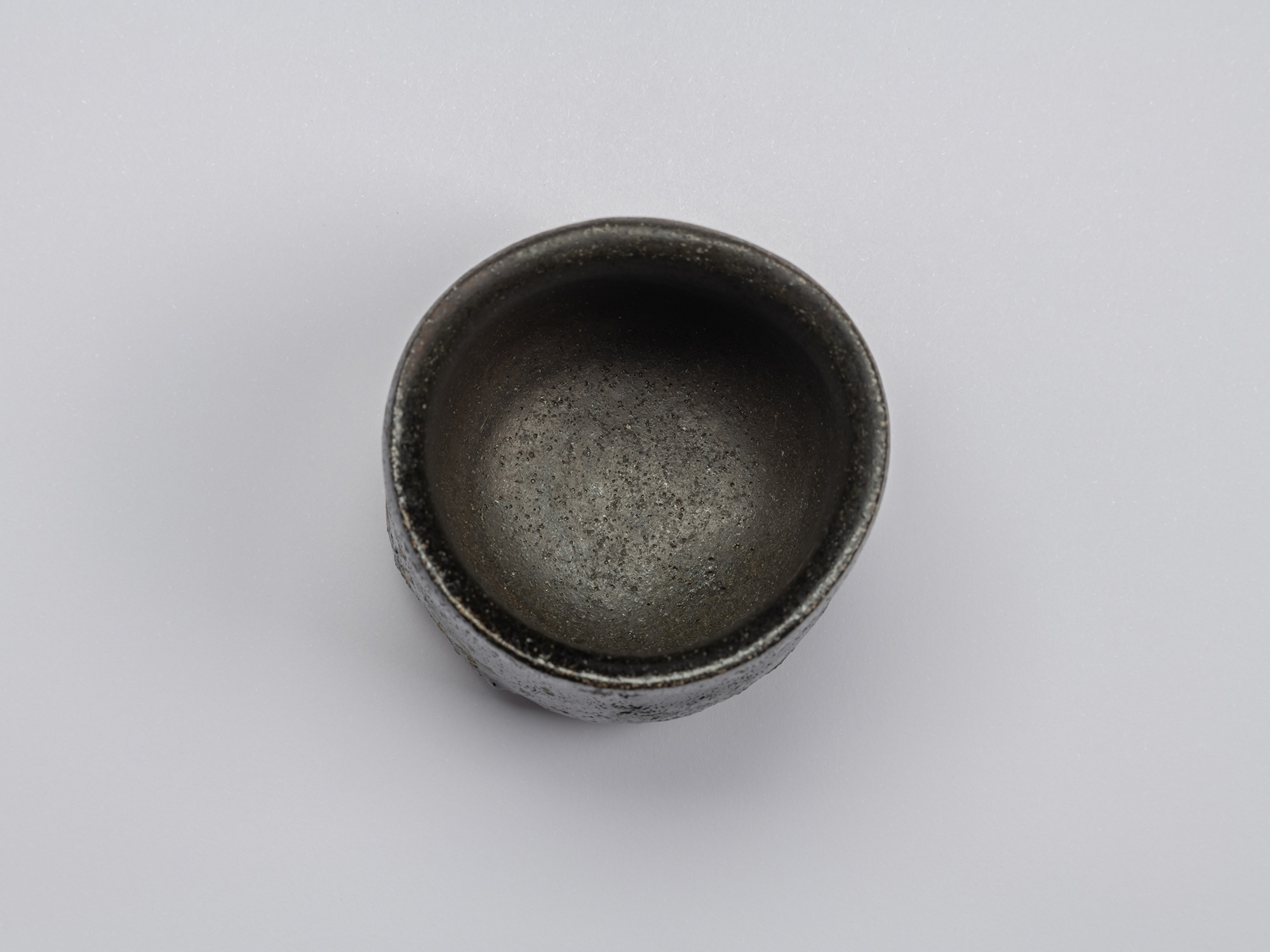 Interior view of Shiro Tsujimura’s Kuro Guinomi, showing a dark black-brown surface with fine pitting,...