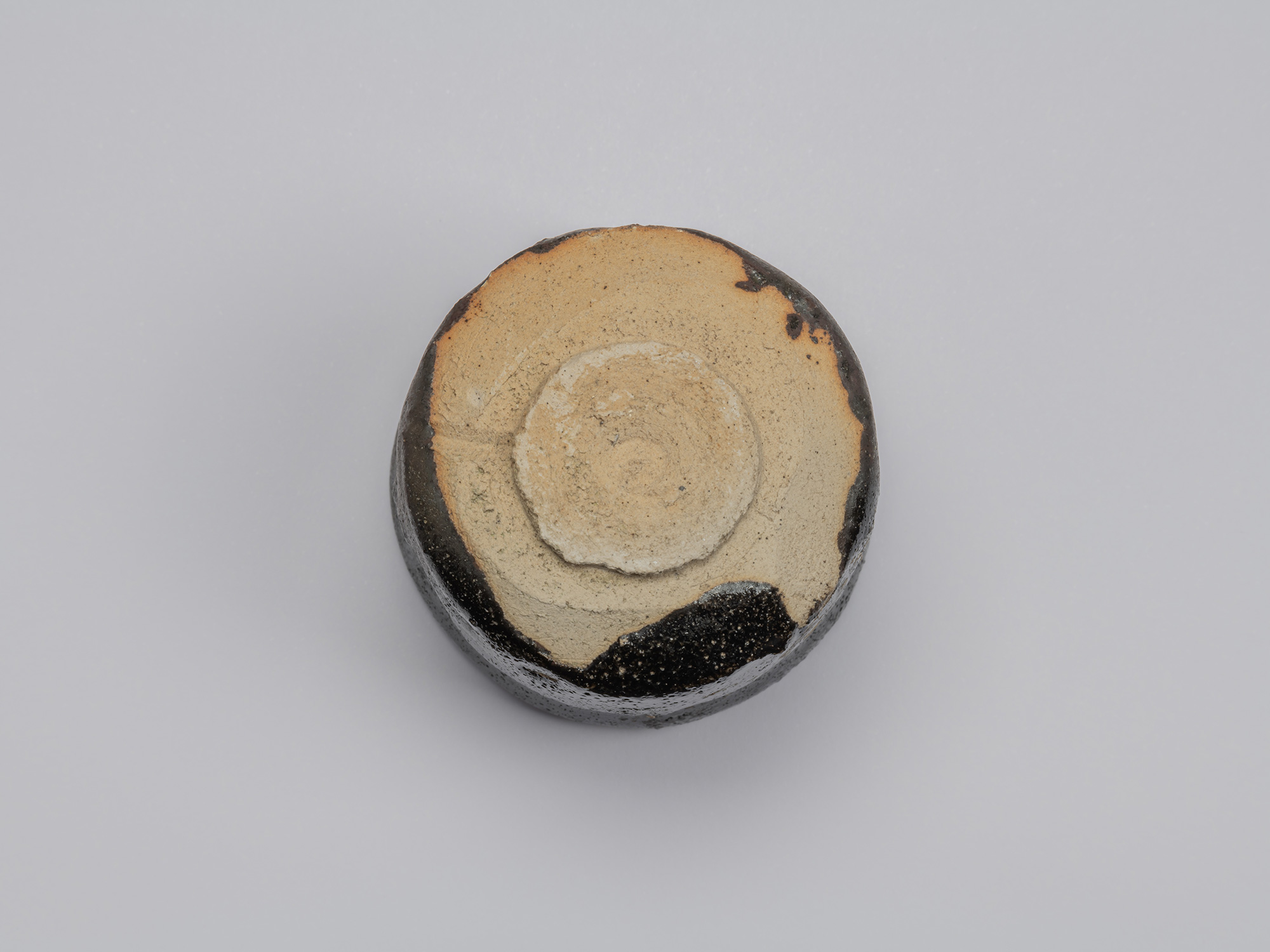 Underside of Shiro Tsujimura’s Kuro Guinomi, showing a broad area of exposed pale clay, a roughly...