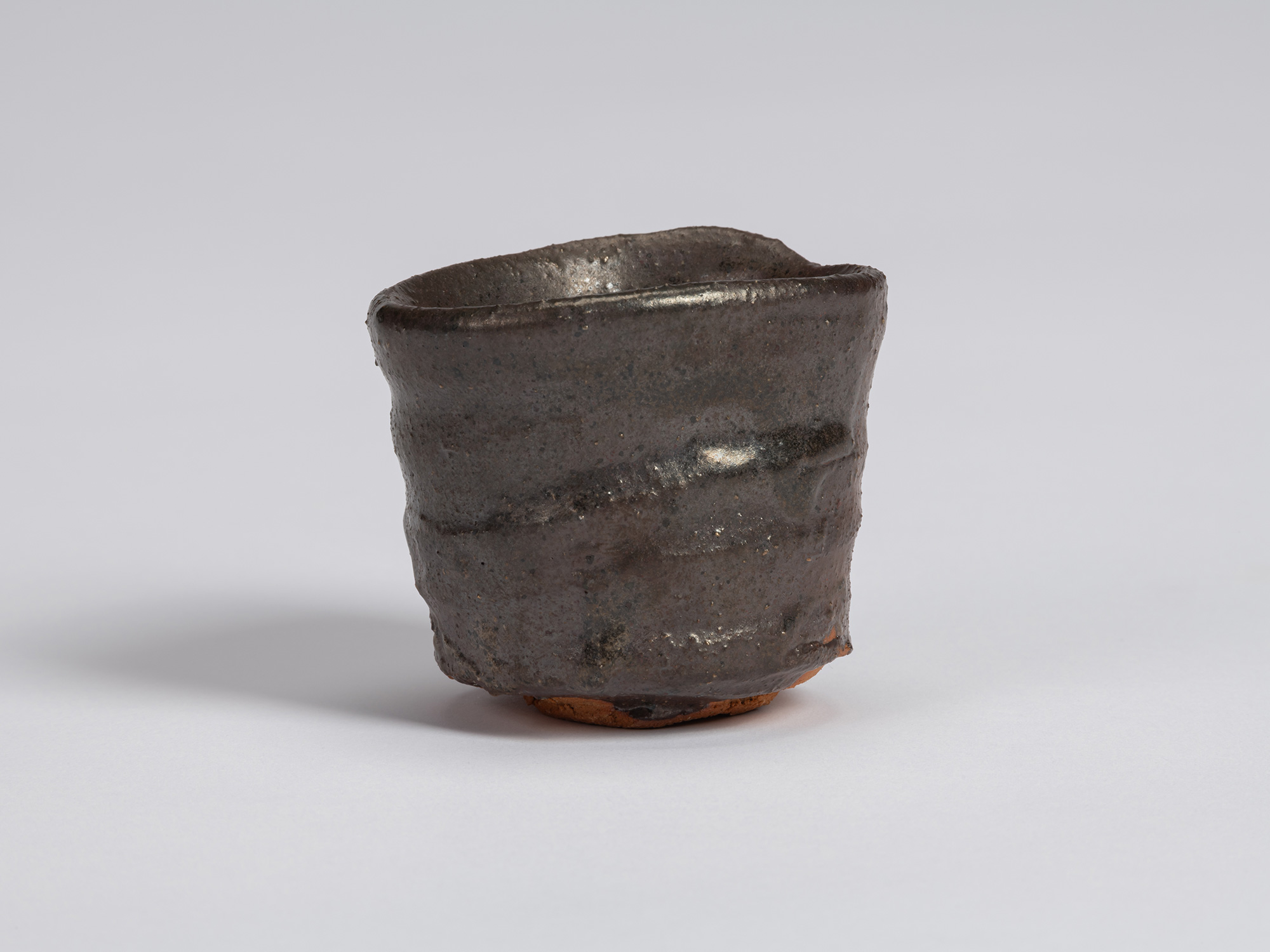 Kuro Guinomi by Shiro Tsujimura, front view, with a cylindrical hand-formed body, uneven rim, and...