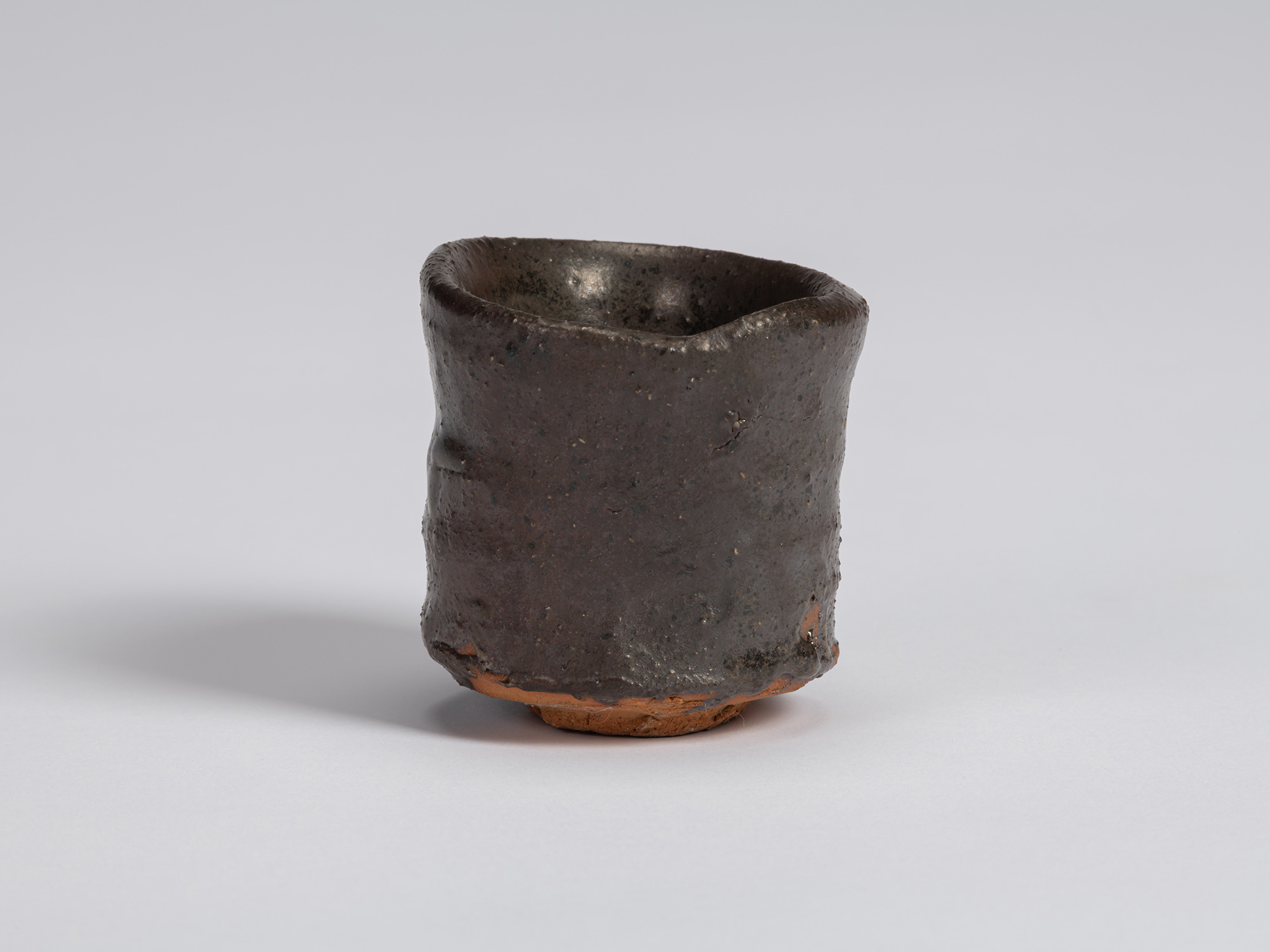Kuro Guinomi by Shiro Tsujimura, front view, with a cylindrical hand-formed body, uneven rim, and...