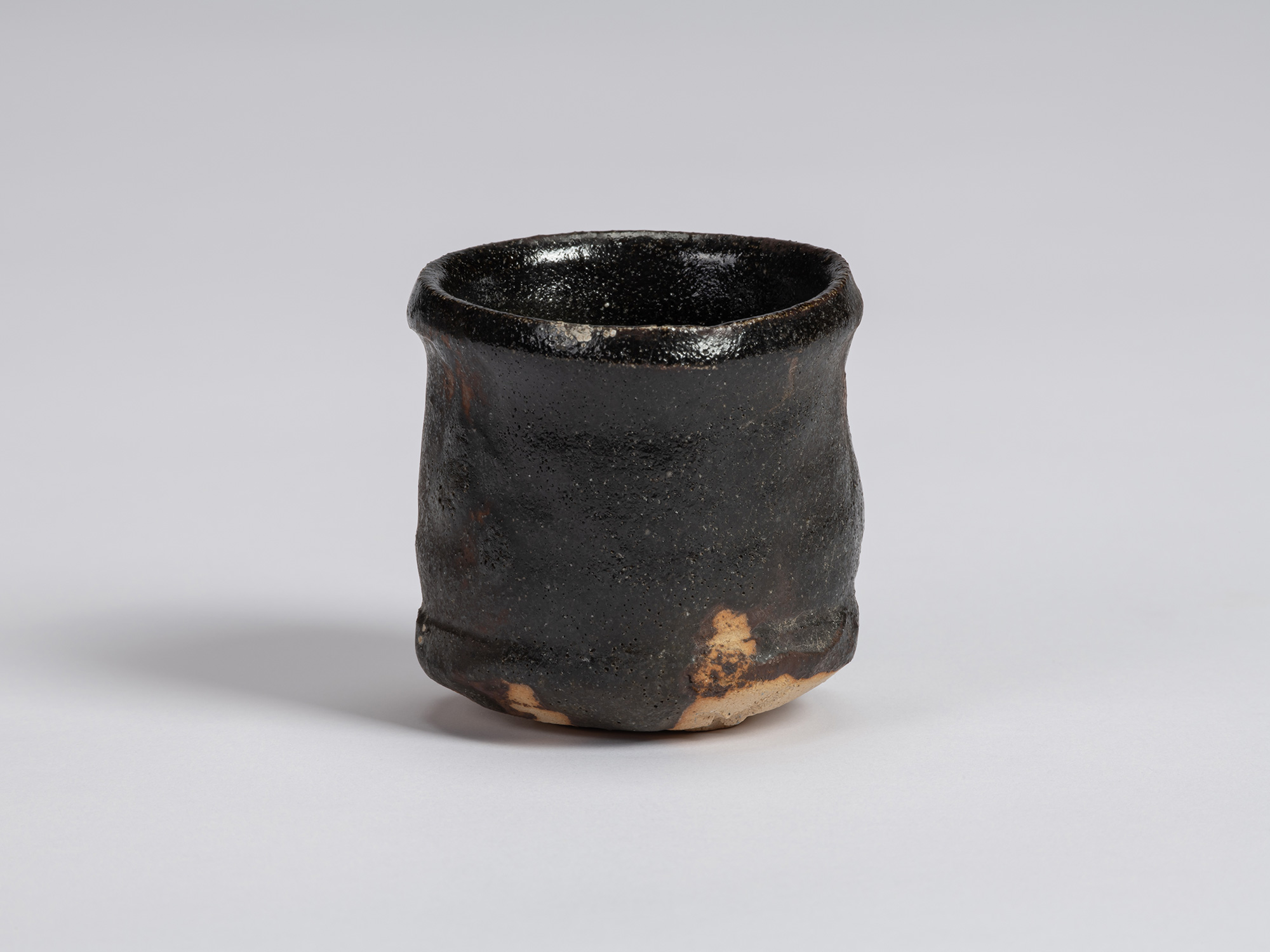 Kuro Guinomi by Shiro Tsujimura with a tall, slightly irregular cylindrical form, textured black...