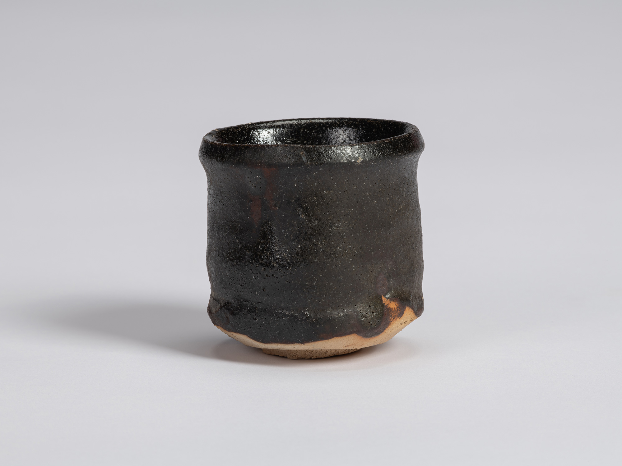 Kuro Guinomi by Shiro Tsujimura with a tall, slightly irregular cylindrical form, textured black...