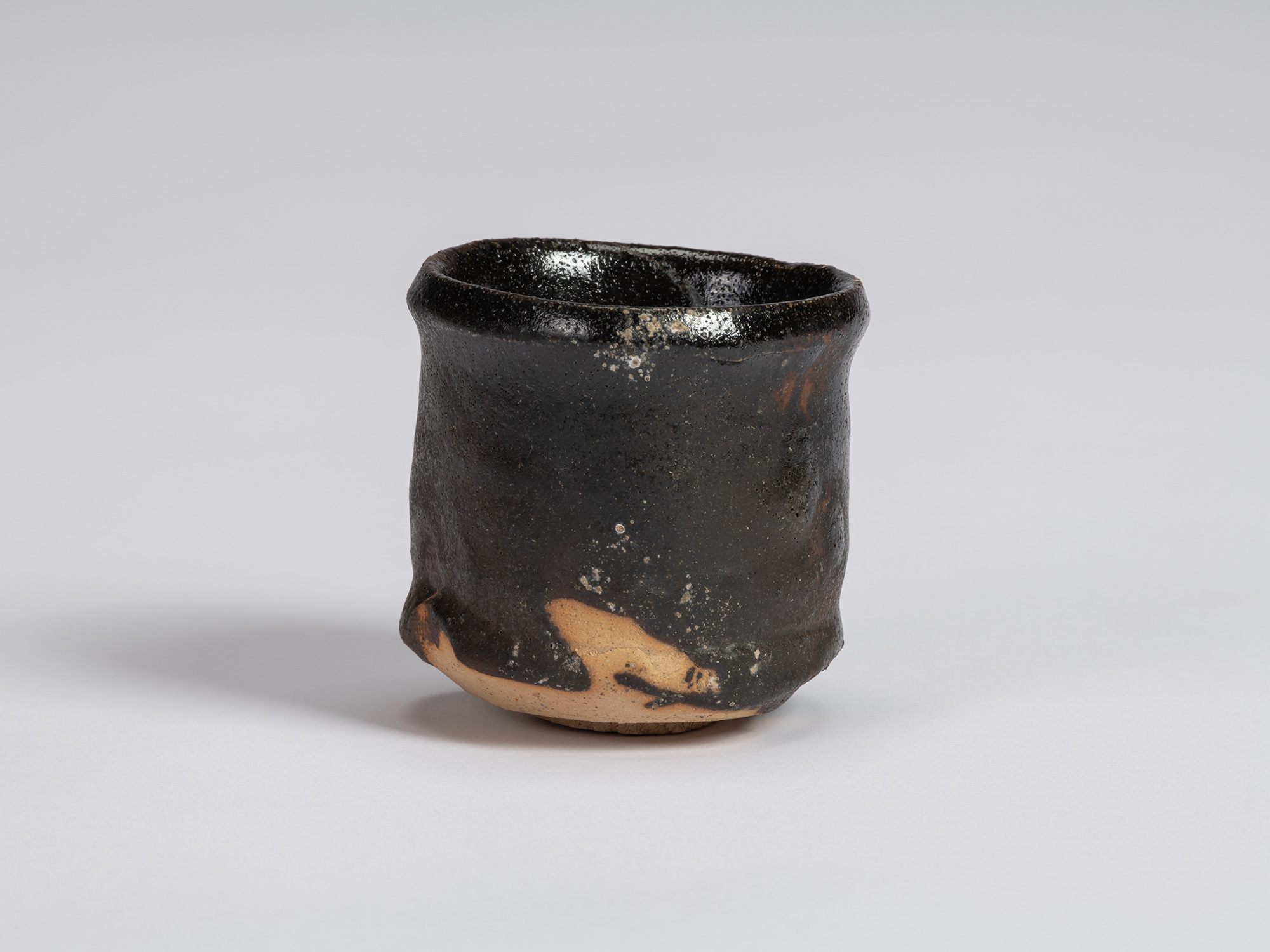 Kuro Guinomi by Shiro Tsujimura with a tall, slightly irregular cylindrical form, textured black...