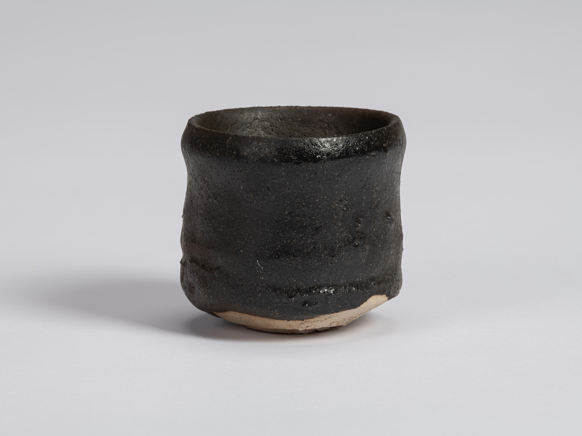 Kuro Guinomi by Shiro Tsujimura with a tall, slightly irregular cylindrical form, textured black...