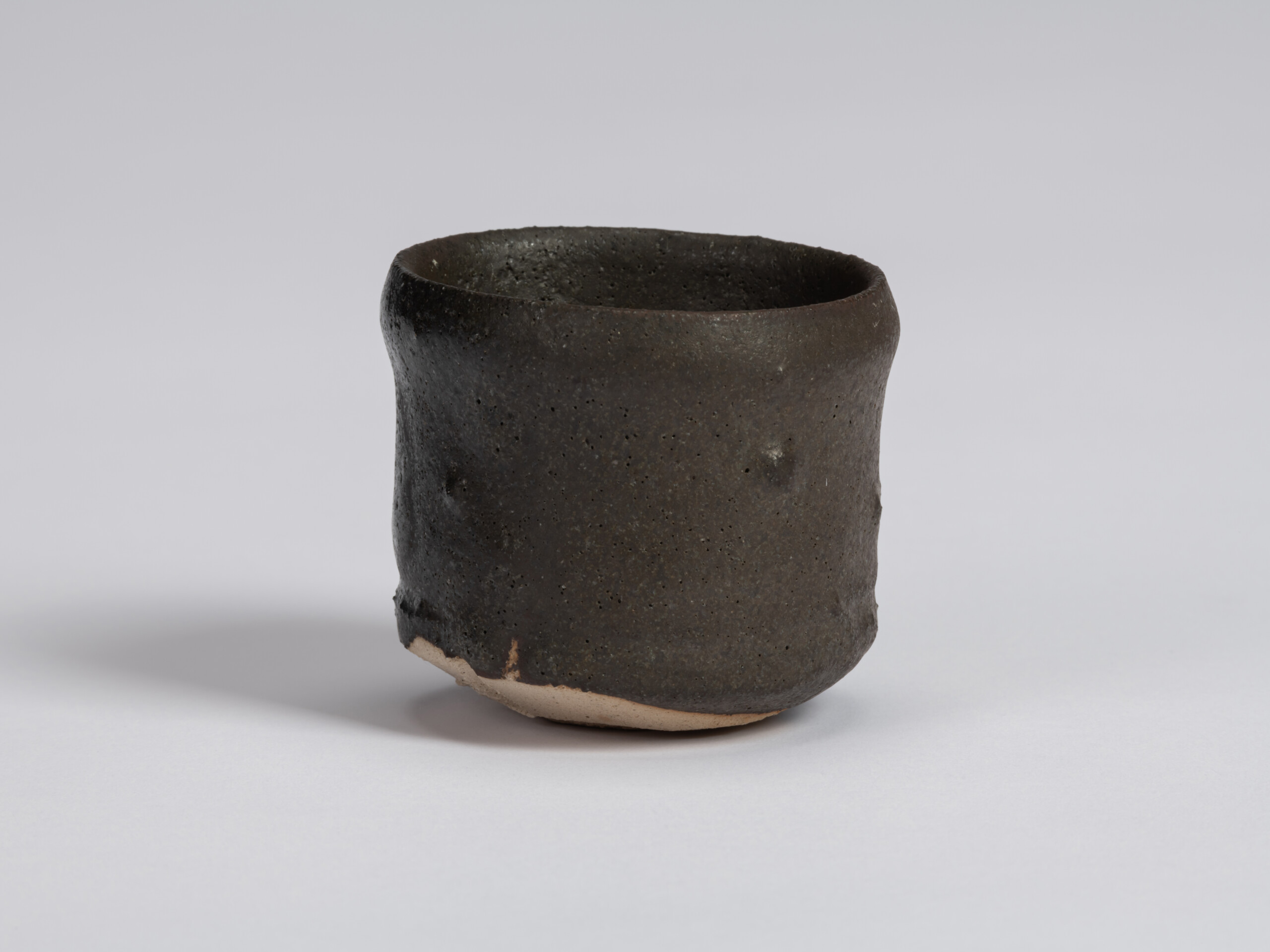 Kuro Guinomi by Shiro Tsujimura with a tall, slightly irregular cylindrical form, textured black...