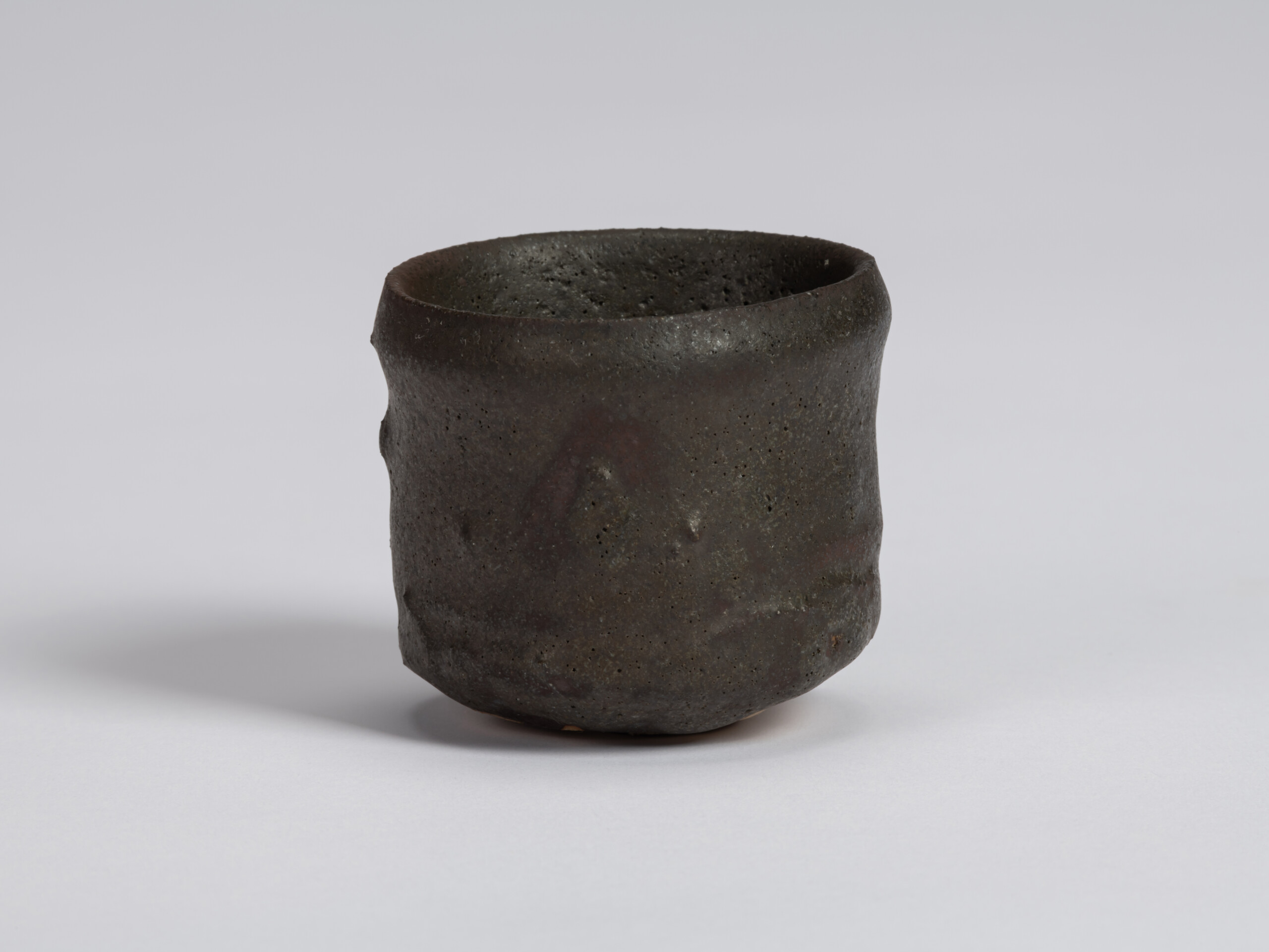 Kuro Guinomi by Shiro Tsujimura with a tall, slightly irregular cylindrical form, textured black...