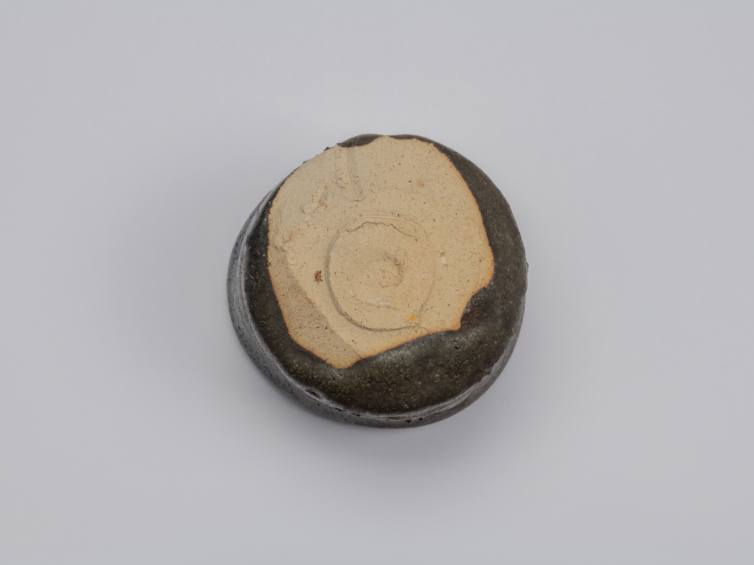 Underside of Shiro Tsujimura’s Kuro Guinomi, showing a broad area of unglazed pale clay with a...