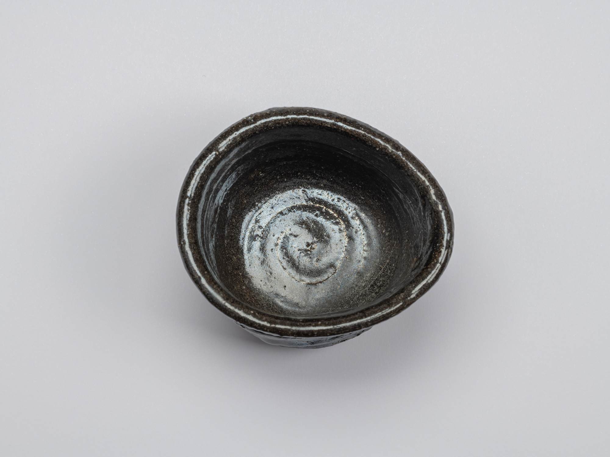 Overhead view of the Kuro Guinomi, showing its irregular rim and dark glazed interior with a prominent...