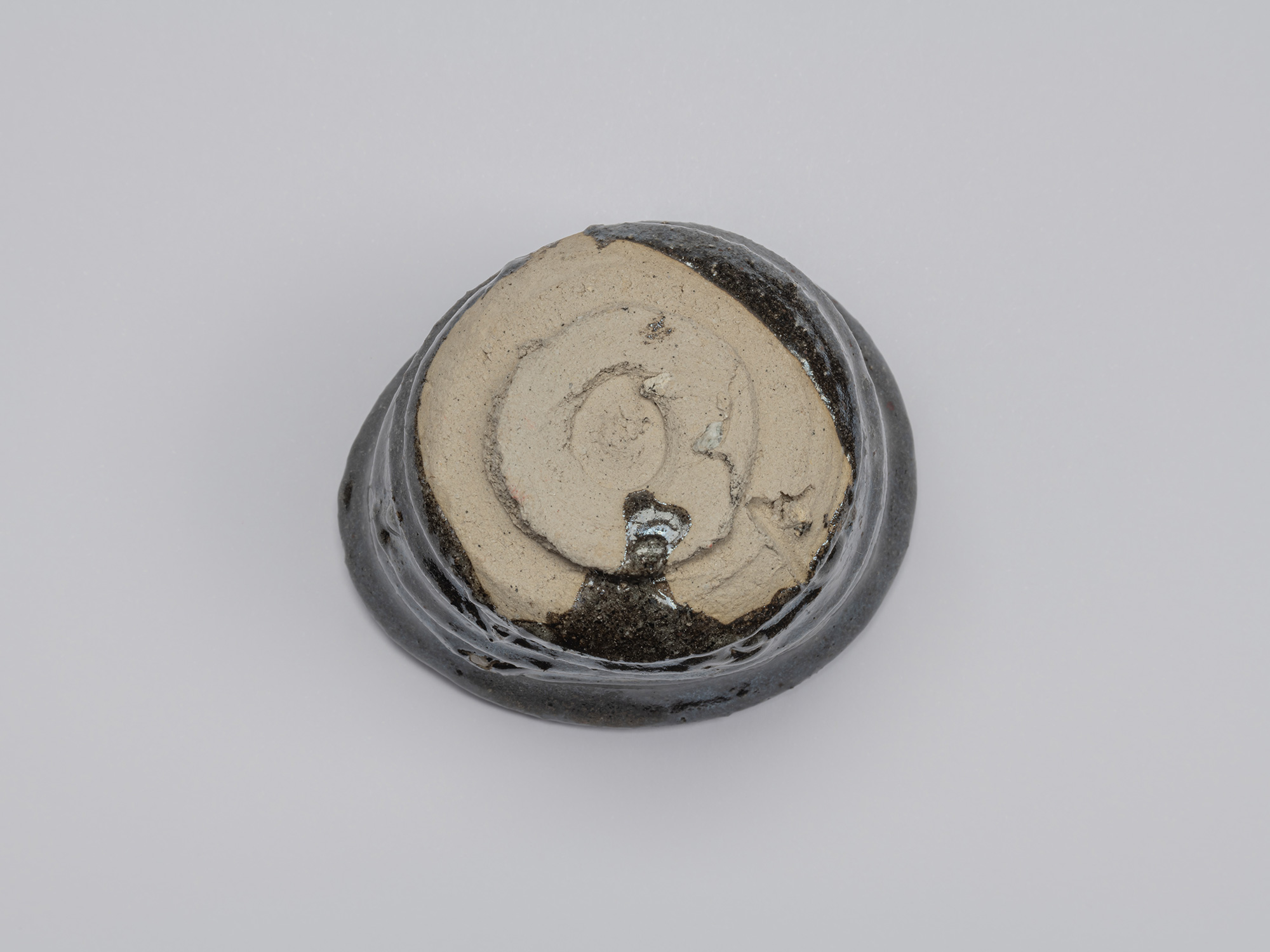 Bottom view of the Kuro Guinomi, showing the circular foot and largely unglazed pale clay base...