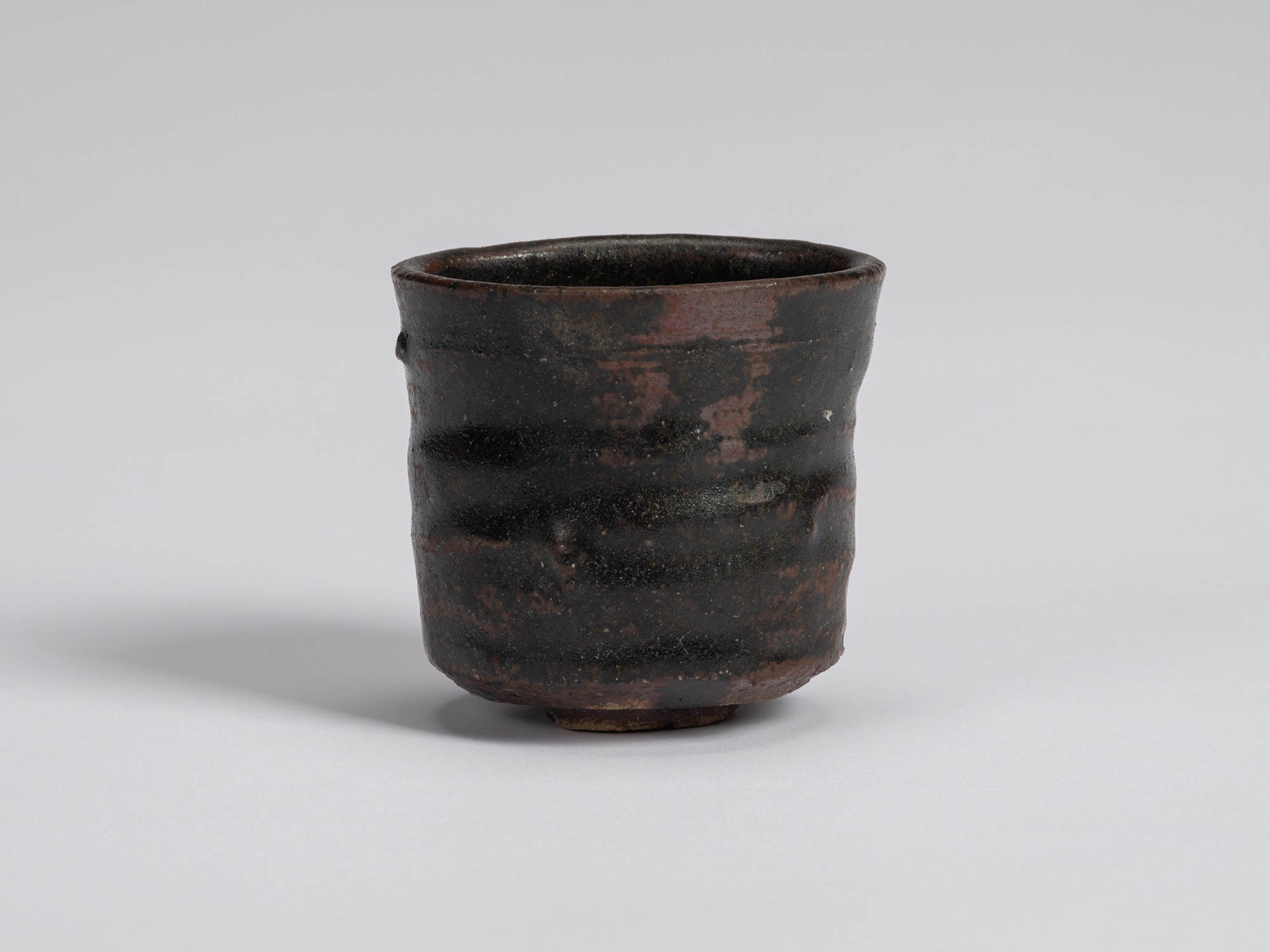 Kuro Guinomi by Shiro Tsujimura, with a cylindrical, slightly irregular form and dark black glaze...