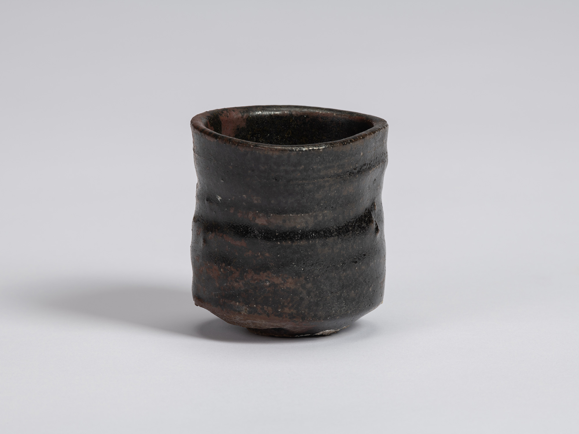 Kuro Guinomi by Shiro Tsujimura, with a cylindrical, slightly irregular form and dark black glaze...