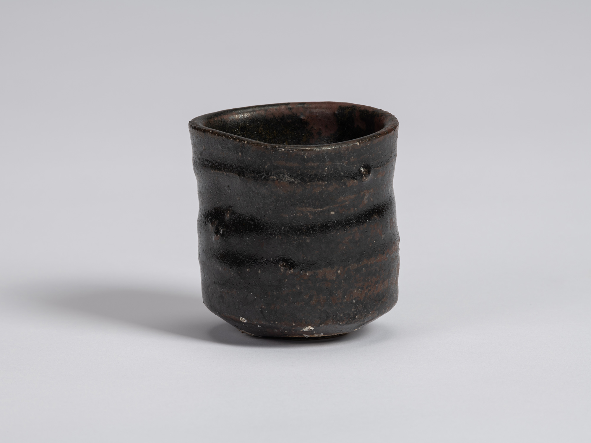 Kuro Guinomi by Shiro Tsujimura, with a cylindrical, slightly irregular form and dark black glaze...