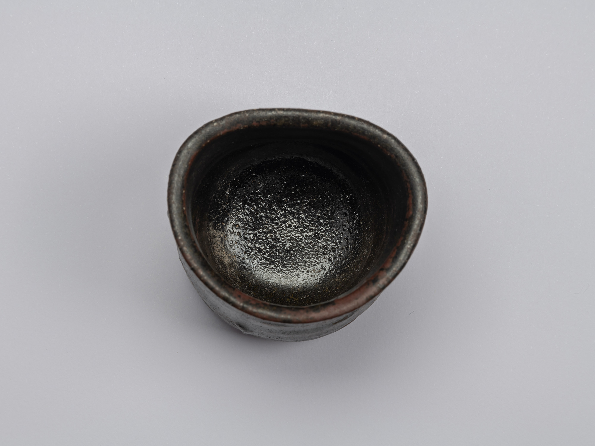 Top view of Kuro Guinomi by Shiro Tsujimura, showing an irregular rounded rim and dark, textured...