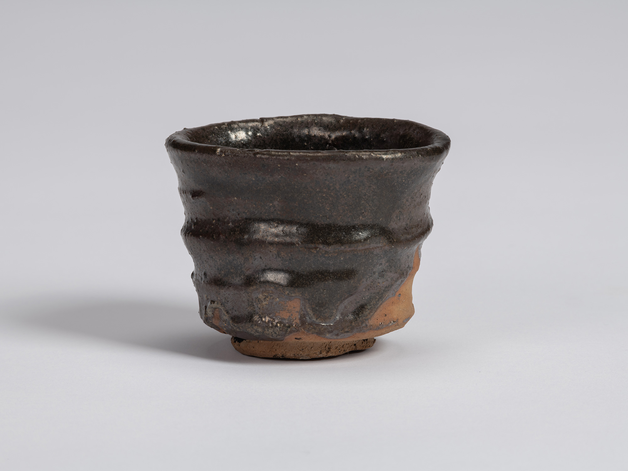 Front view of a Kuro Guinomi by Shiro Tsujimura, with a tall, slightly waisted cylindrical form,...