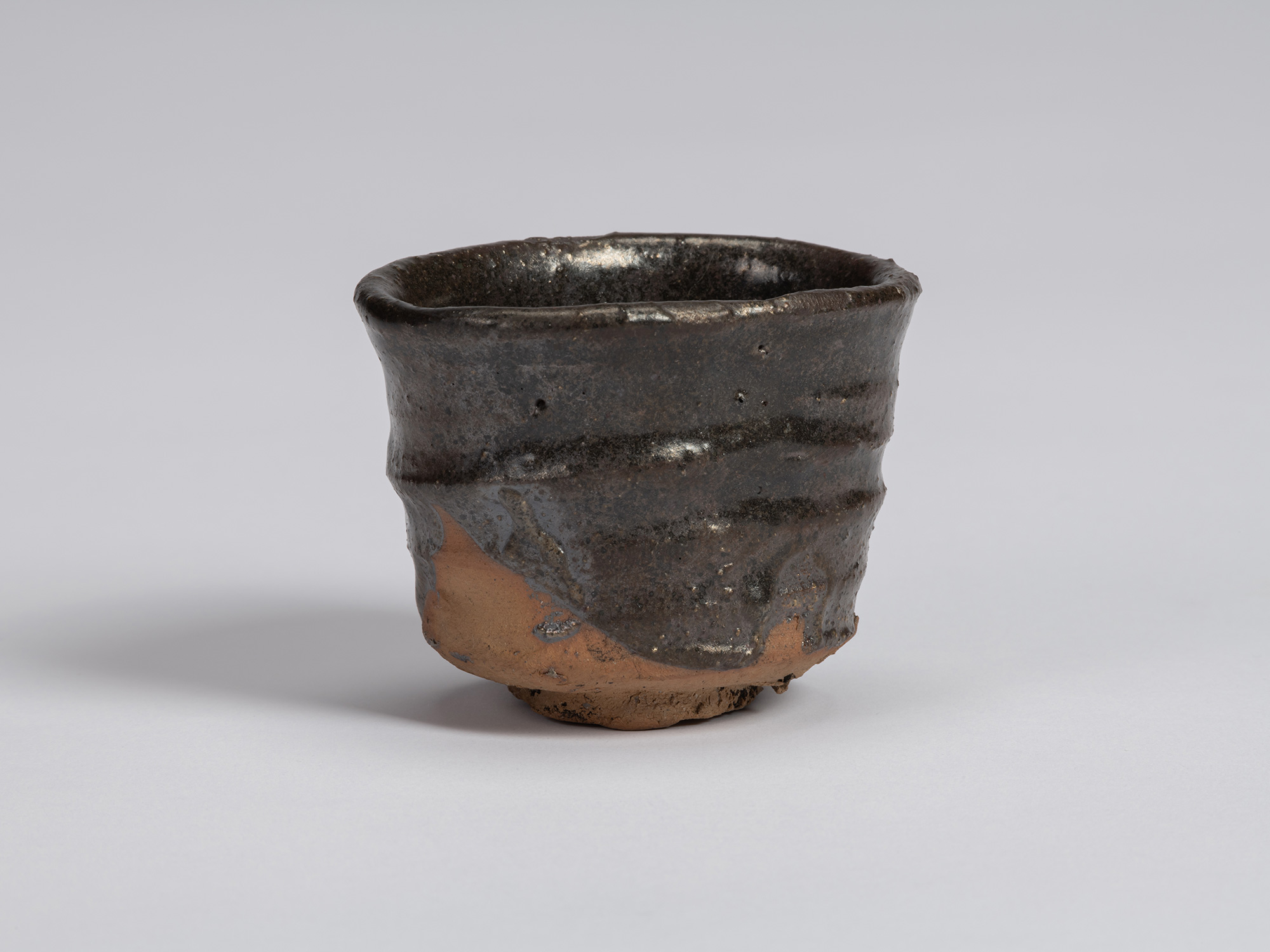Front view of a Kuro Guinomi by Shiro Tsujimura, with a tall, slightly waisted cylindrical form,...