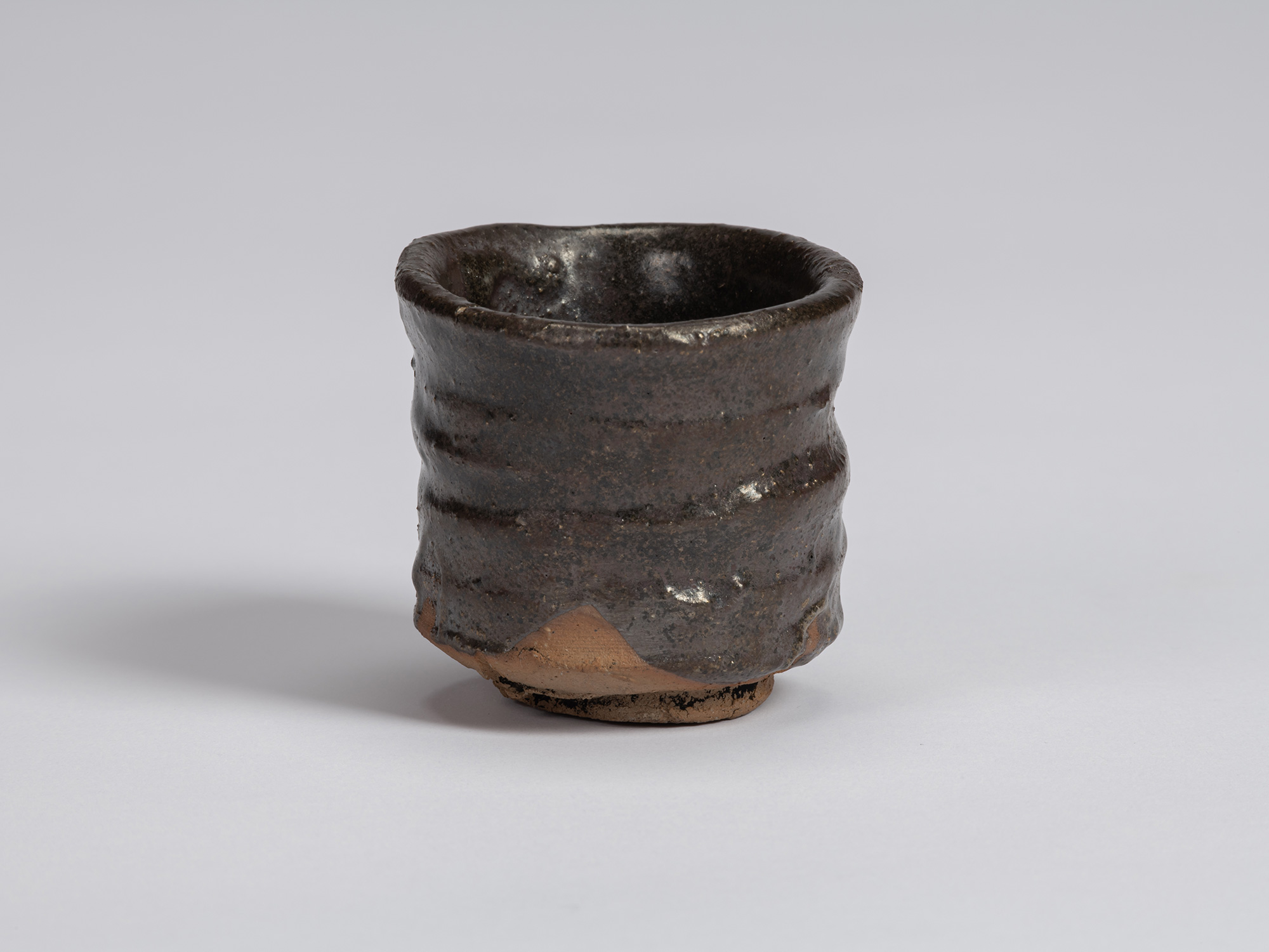 Front view of a Kuro Guinomi by Shiro Tsujimura, with a tall, slightly waisted cylindrical form,...