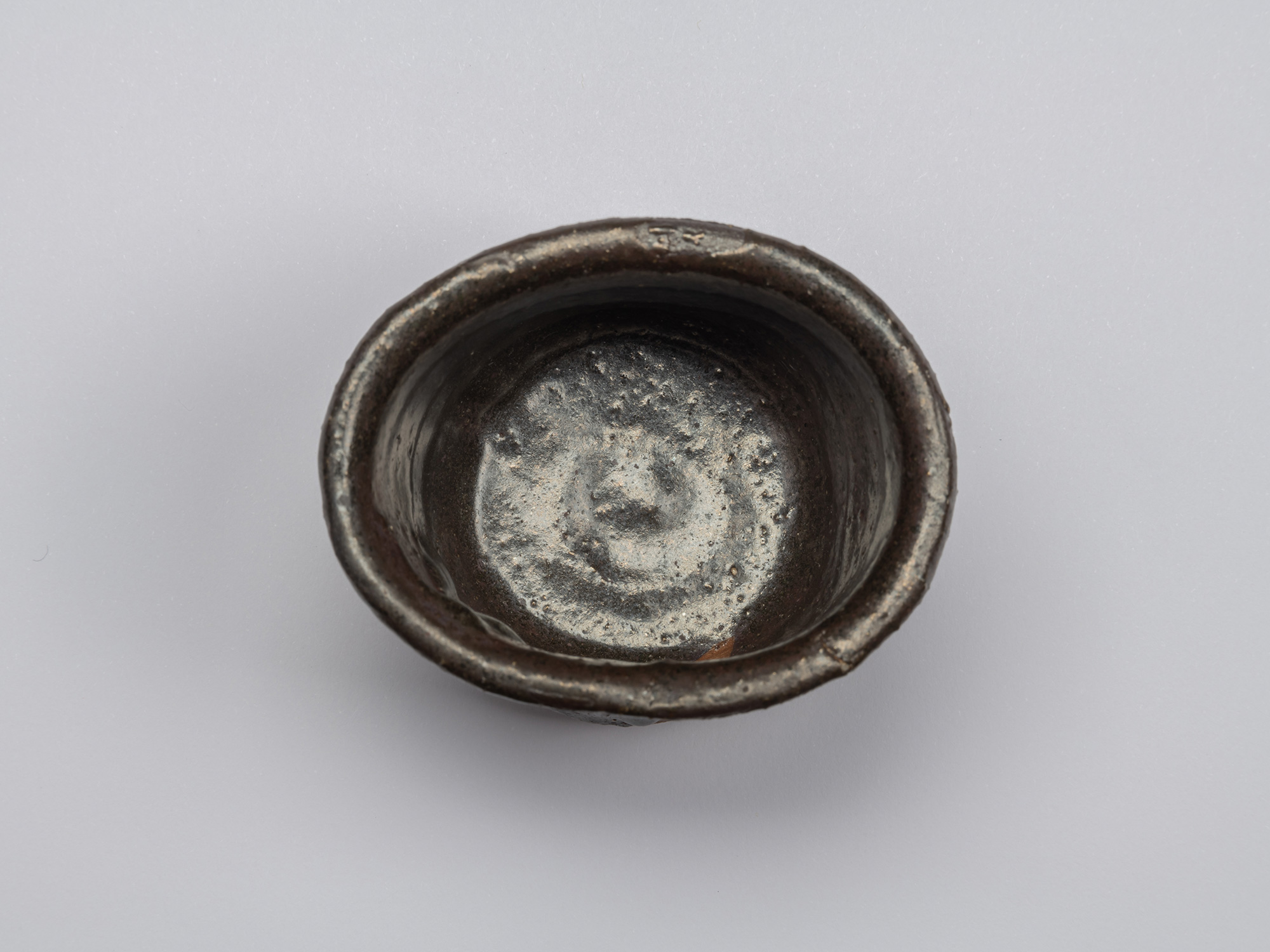 Overhead view of the Kuro Guinomi, showing the rounded rim and dark interior with a subtly textured...