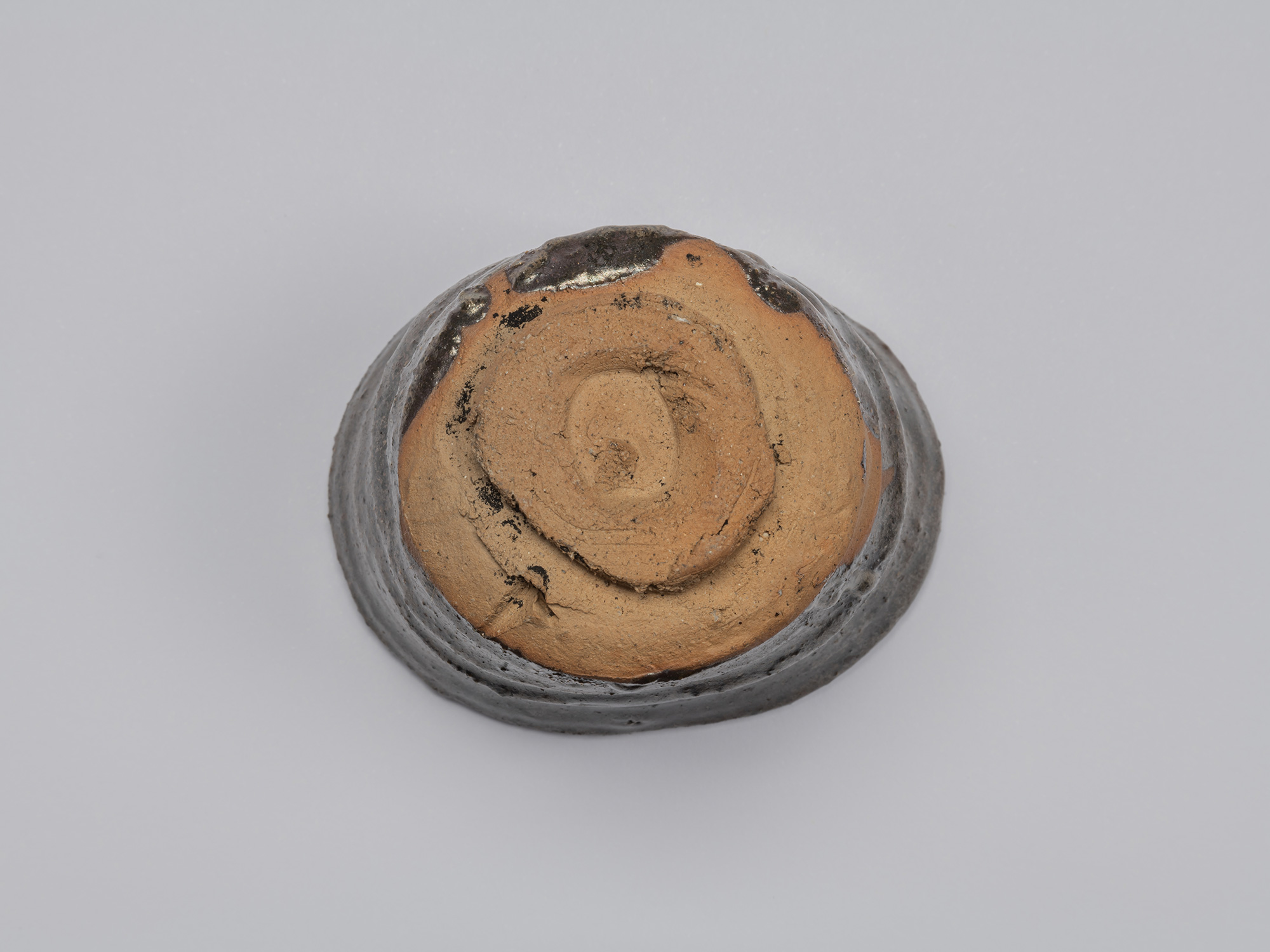 Bottom view of the Kuro Guinomi, showing the roughly formed circular foot with exposed reddish-brown...