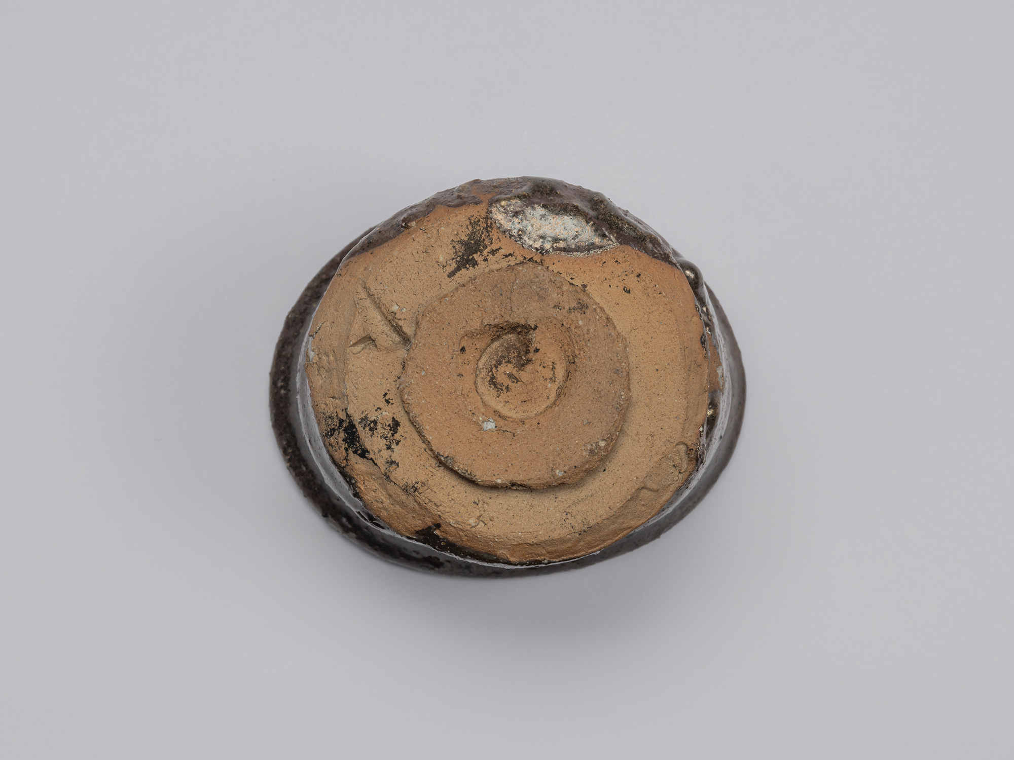 Underside of Shiro Tsujimura’s kuro guinomi showing an unglazed reddish-brown clay base, roughly...