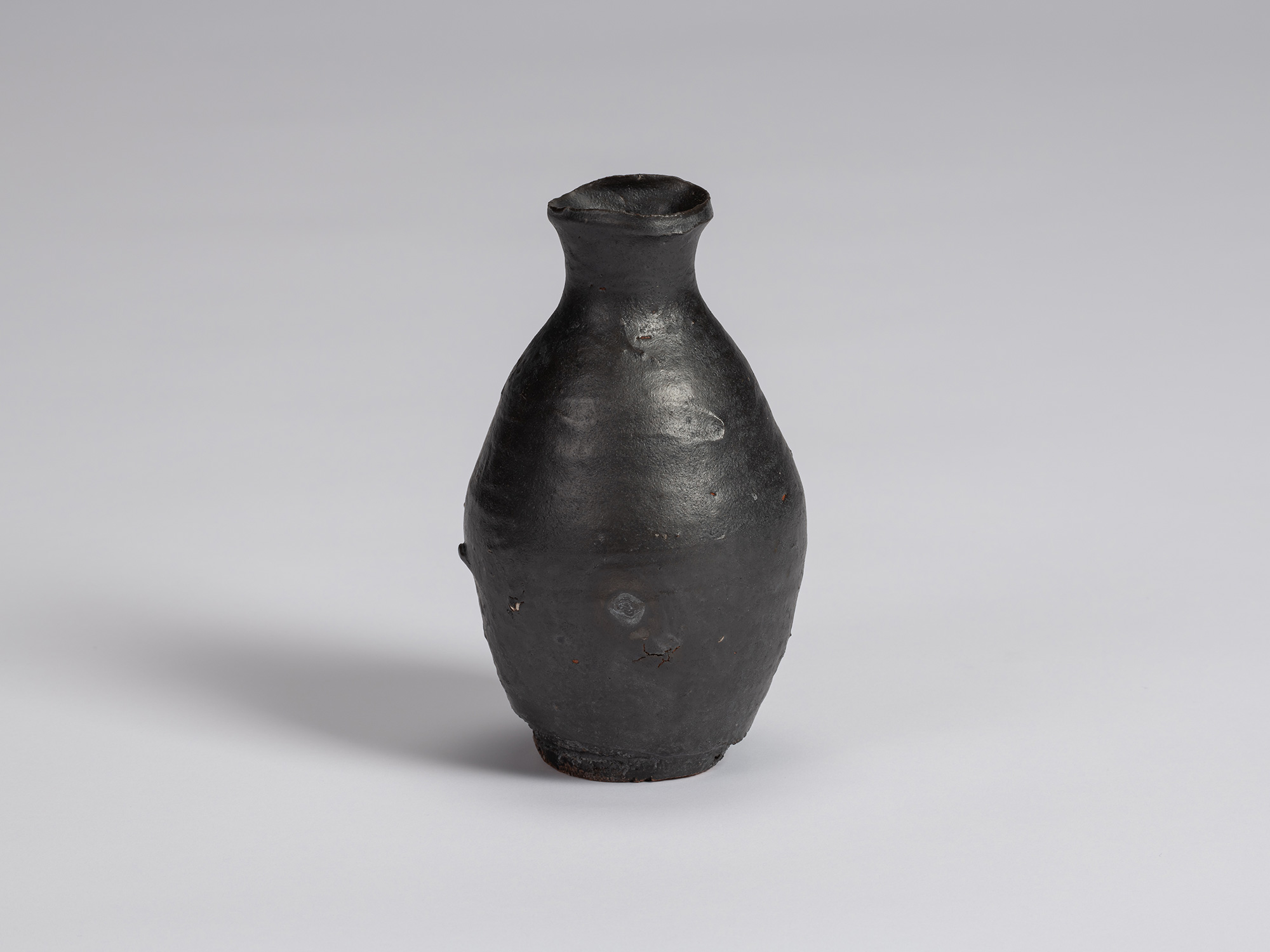 Kuro tokkuri by Shiro Tsujimura with a rounded, slightly asymmetrical body, narrow neck, and irregular...