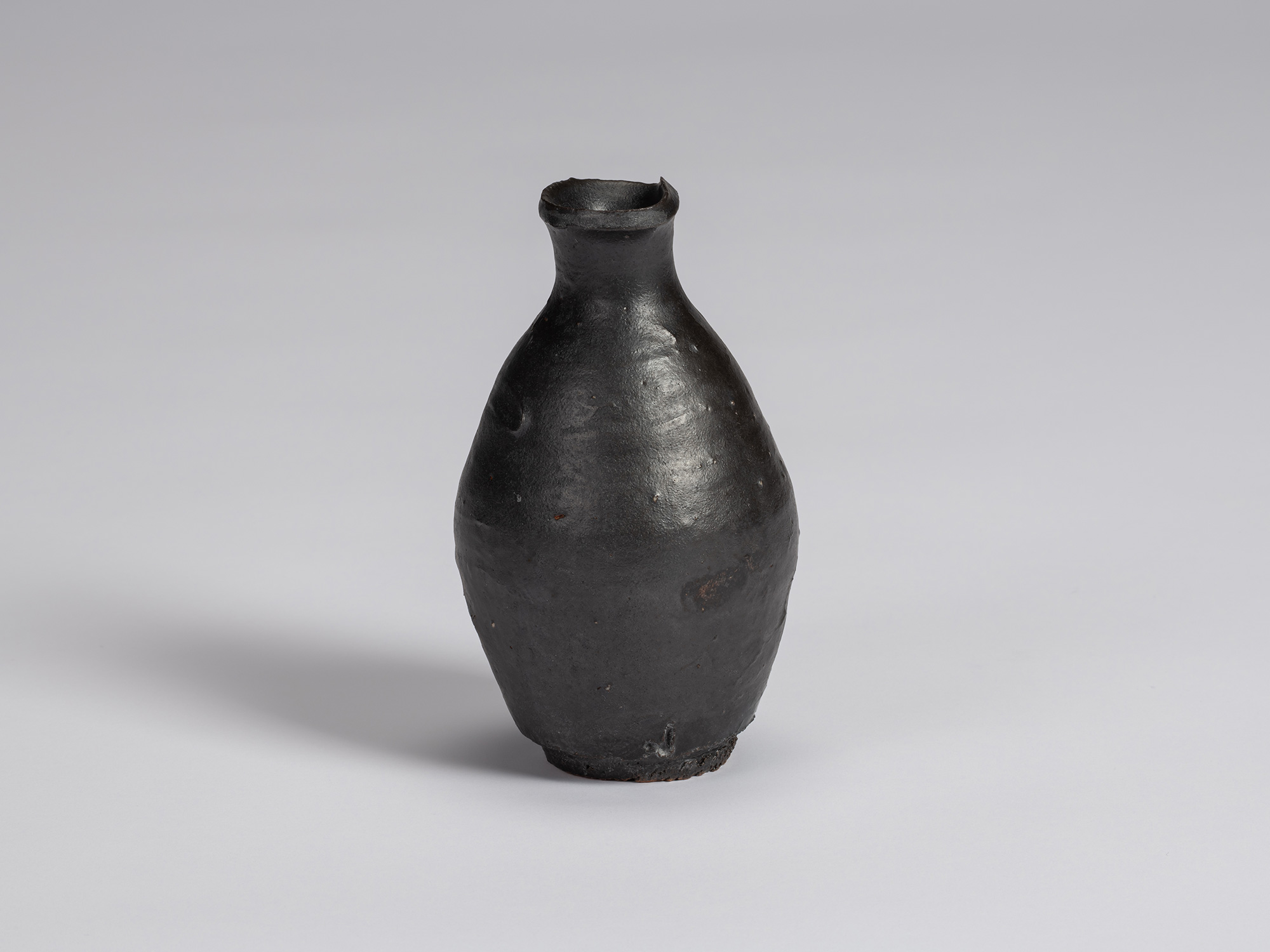 Kuro tokkuri by Shiro Tsujimura with a rounded, slightly asymmetrical body, narrow neck, and irregular...