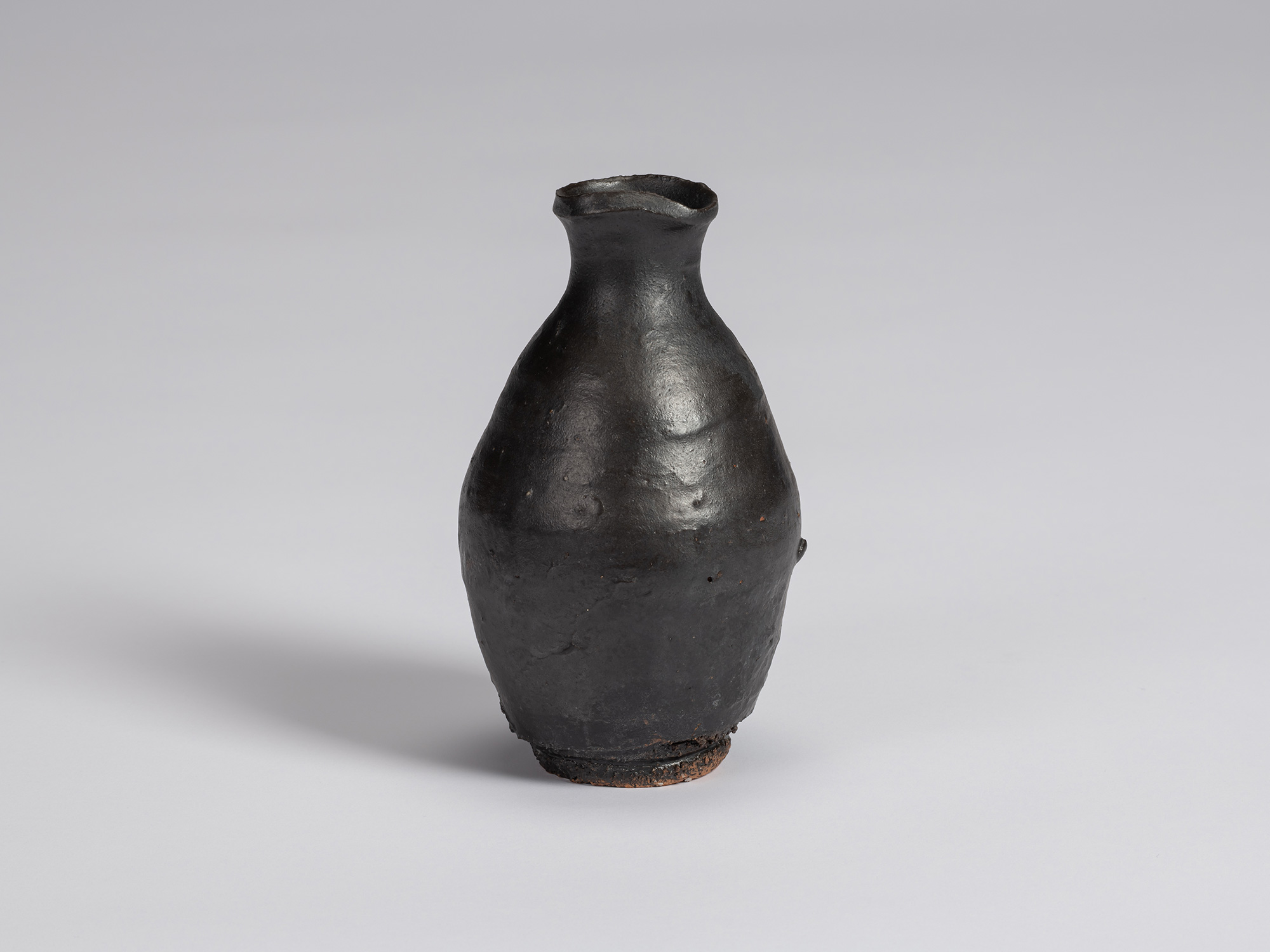 Kuro tokkuri by Shiro Tsujimura with a rounded, slightly asymmetrical body, narrow neck, and irregular...
