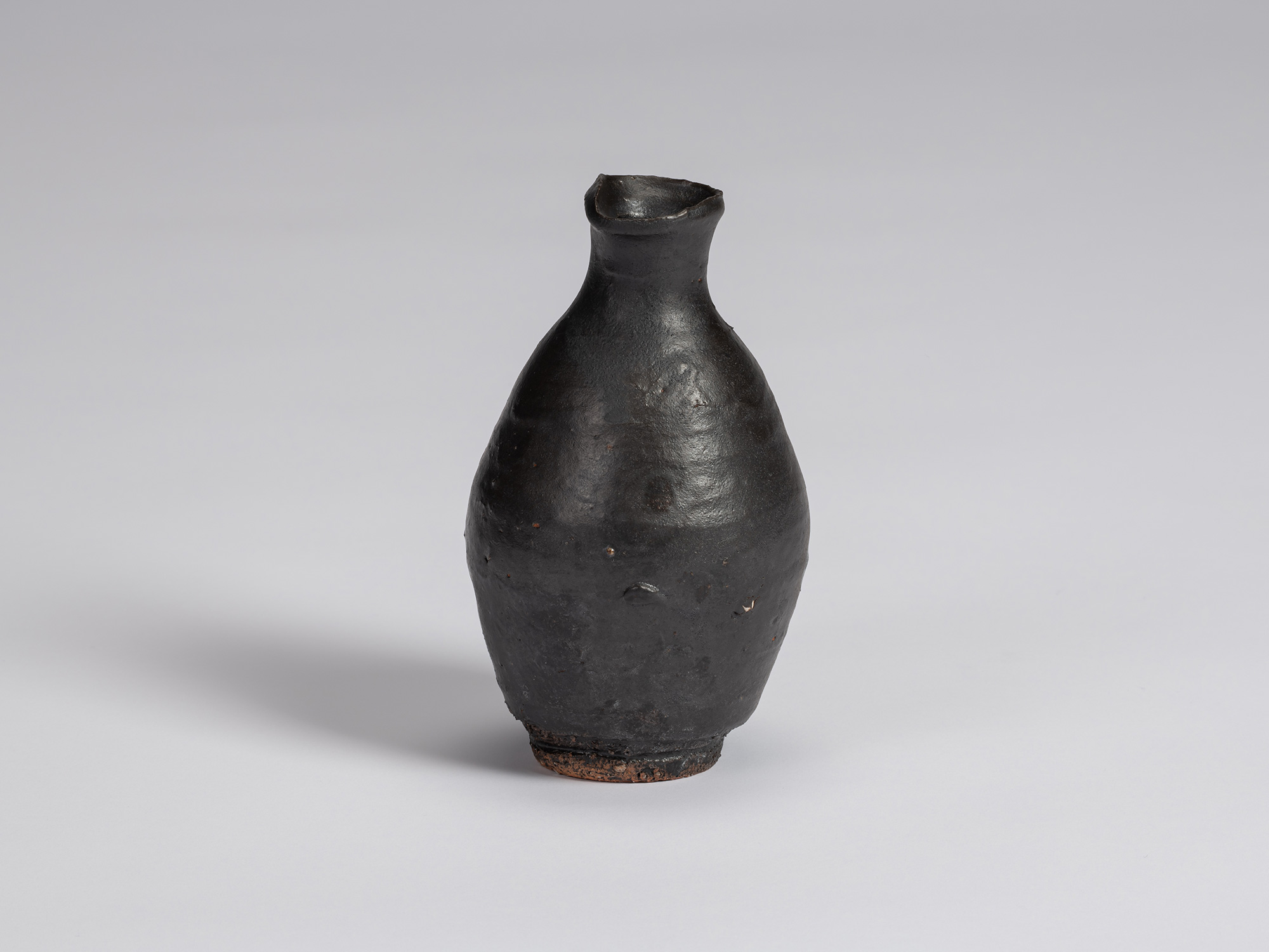 Kuro tokkuri by Shiro Tsujimura with a rounded, slightly asymmetrical body, narrow neck, and irregular...