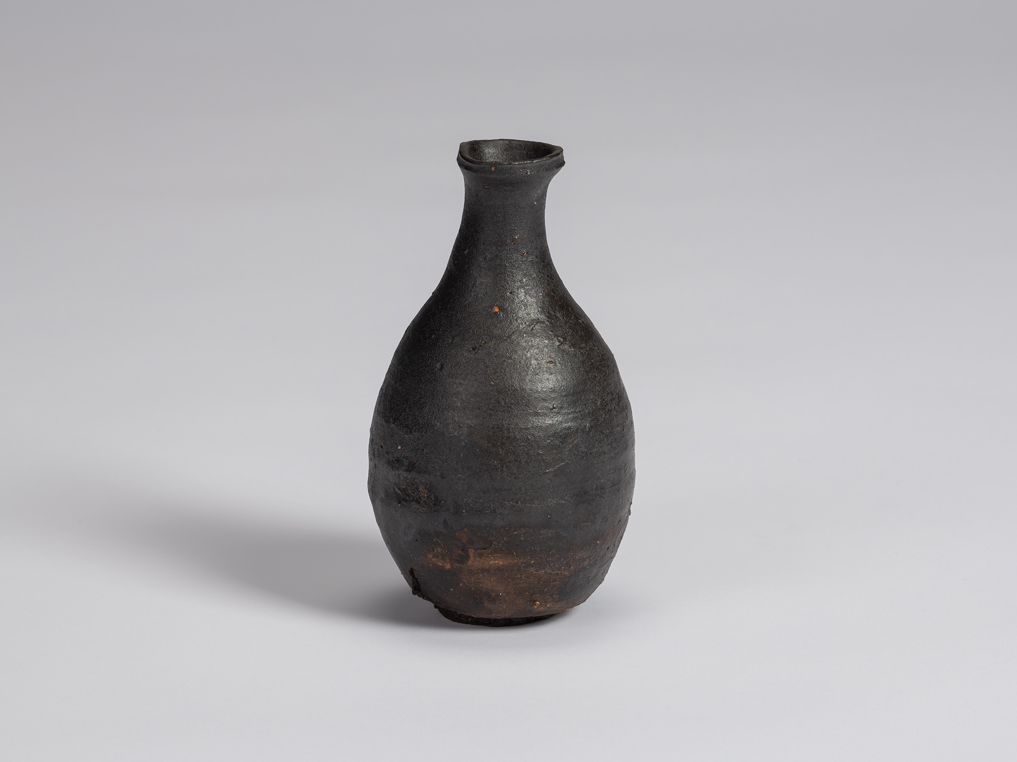 Kuro Tokkuri by Shiro Tsujimura, with a full, pear-shaped body, narrow neck, and irregular flared...