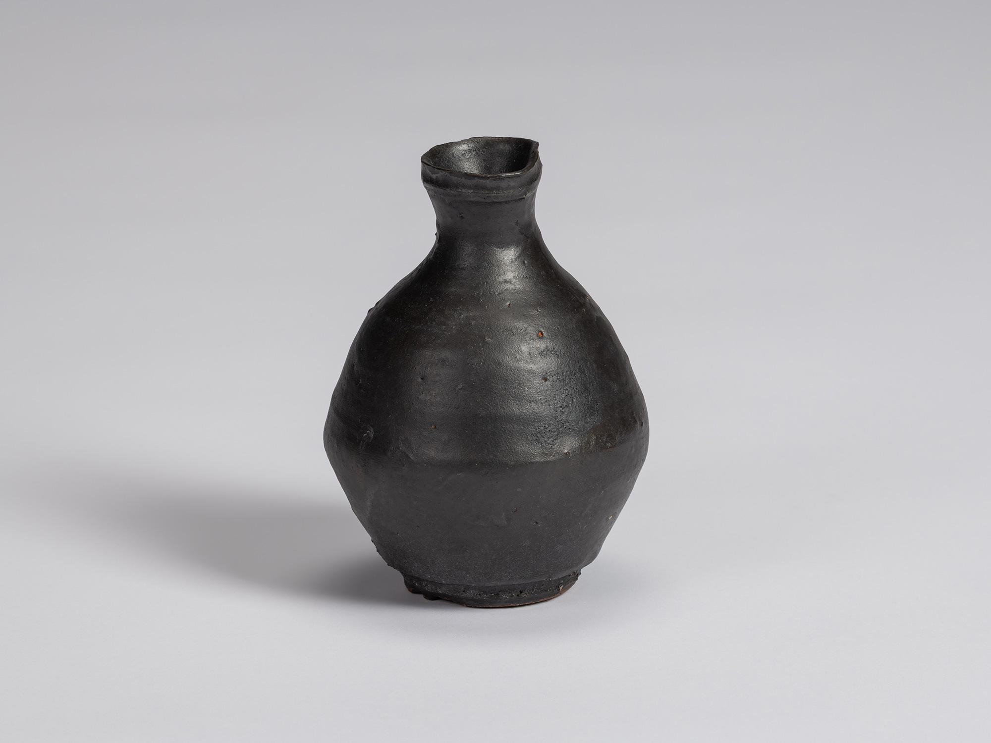 Kuro Tokkuri by Shiro Tsujimura, with a plump, rounded body, short narrow neck, and irregular flared...