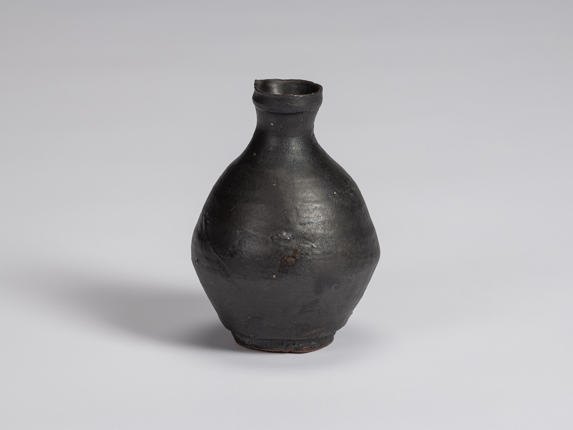 Kuro Tokkuri by Shiro Tsujimura, with a plump, rounded body, short narrow neck, and irregular flared...