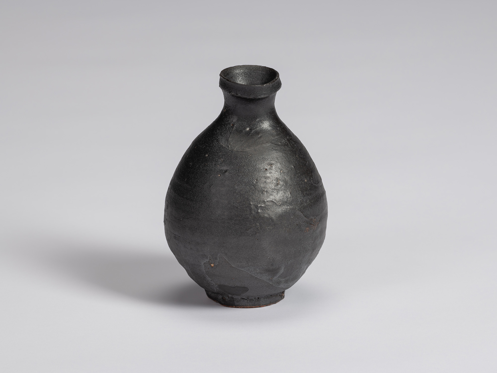 Kuro Tokkuri by Shiro Tsujimura, with a full oval body, short narrow neck, and irregular flared...