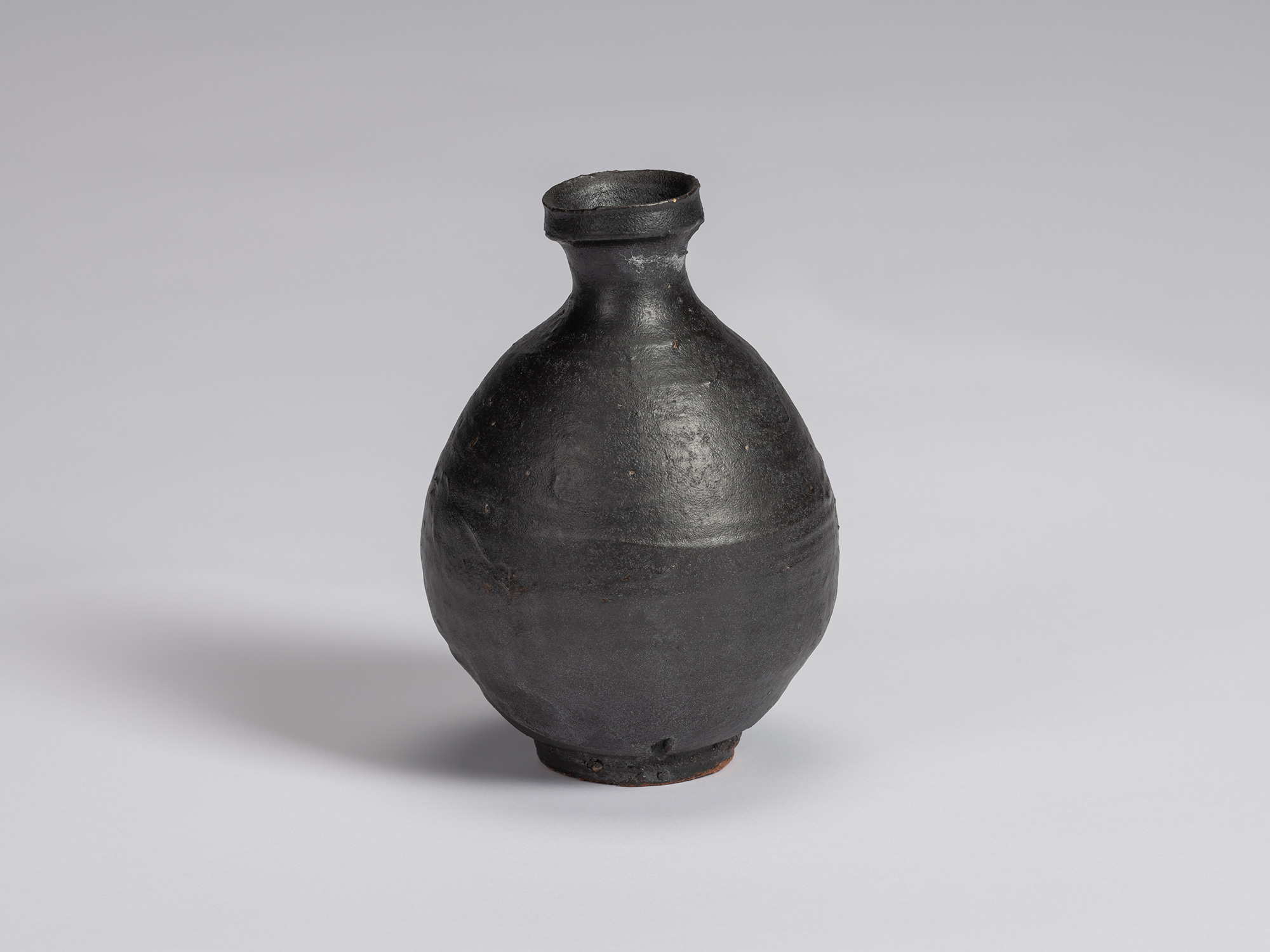 Kuro Tokkuri by Shiro Tsujimura, with a full oval body, short narrow neck, and irregular flared...