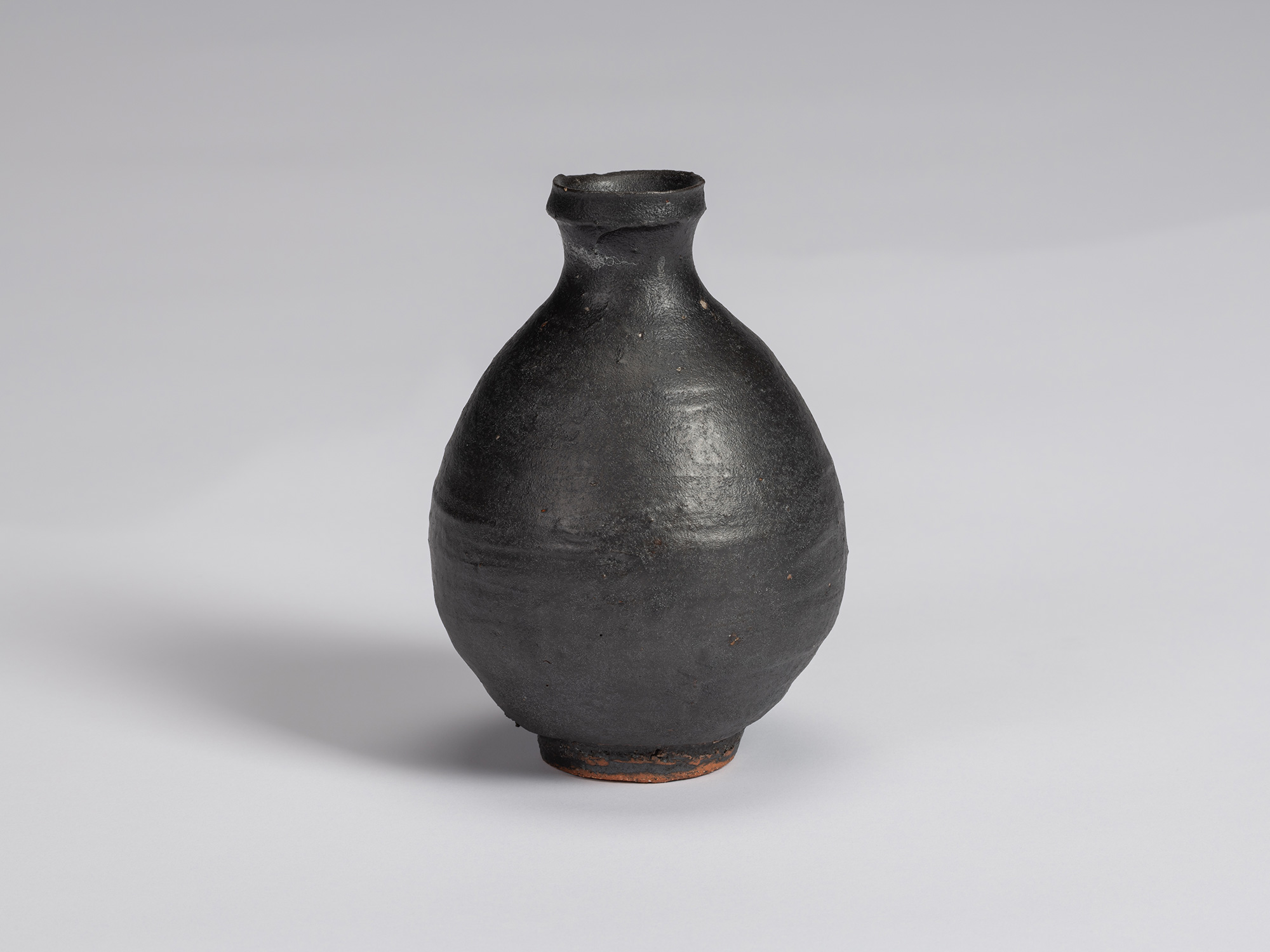 Kuro Tokkuri by Shiro Tsujimura, with a full oval body, short narrow neck, and irregular flared...